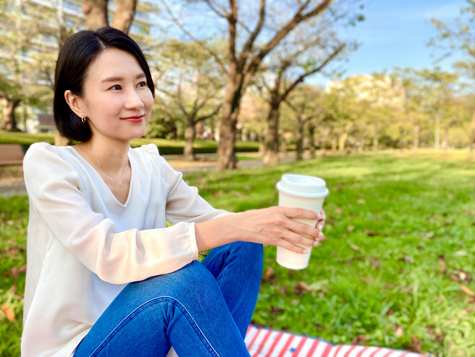 公园里坐着的女性手持咖啡杯，表情平静，背景是树木