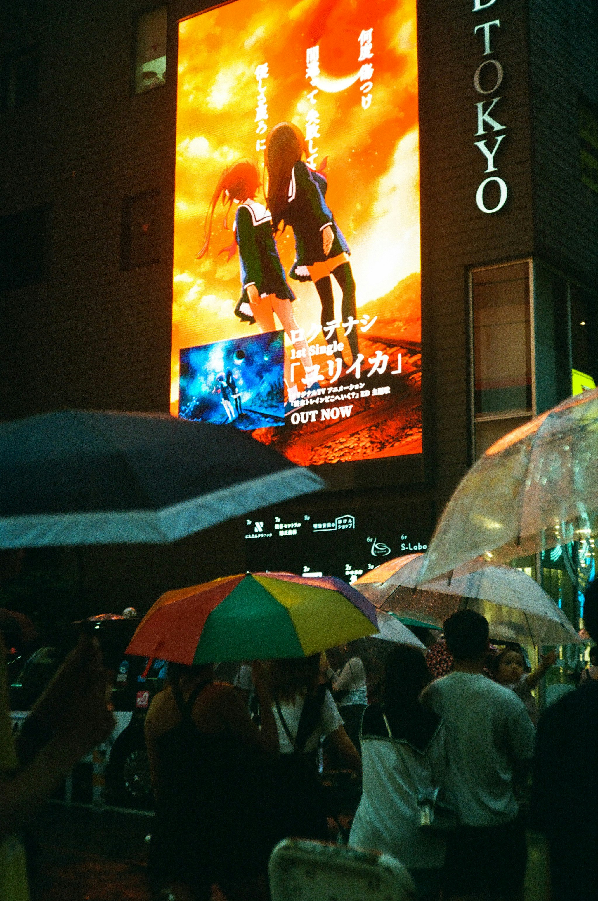 夜の屋外で傘をさす人々と大きな映画館の看板が見える通り
