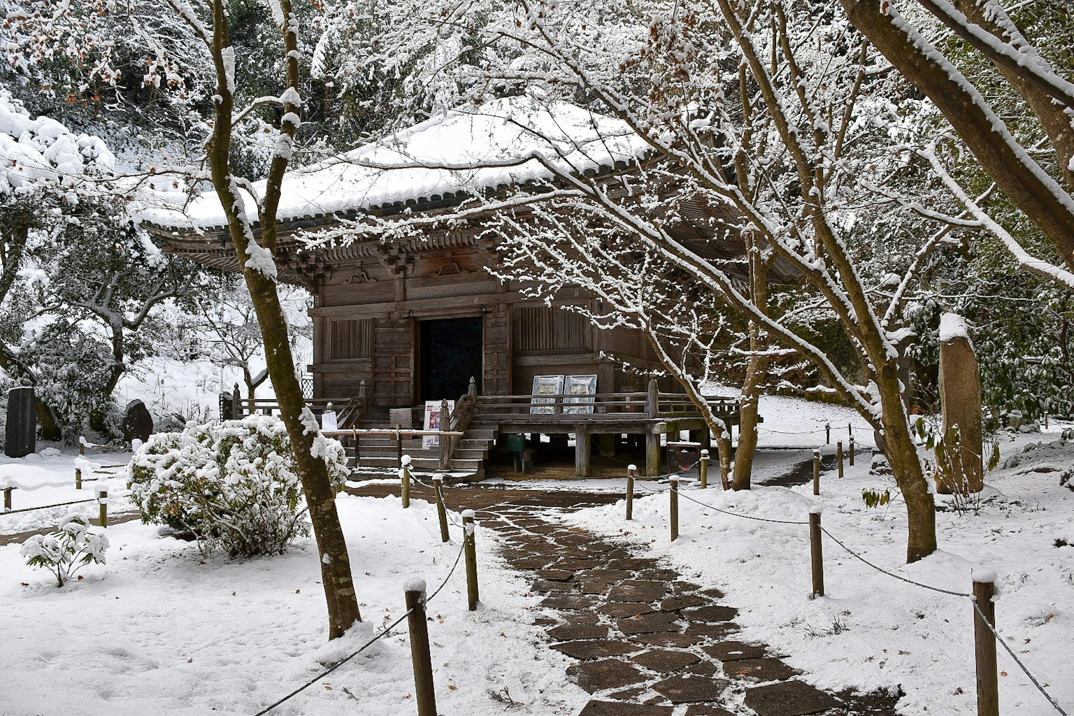 Bâtiment japonais traditionnel couvert de neige avec un chemin en pierre