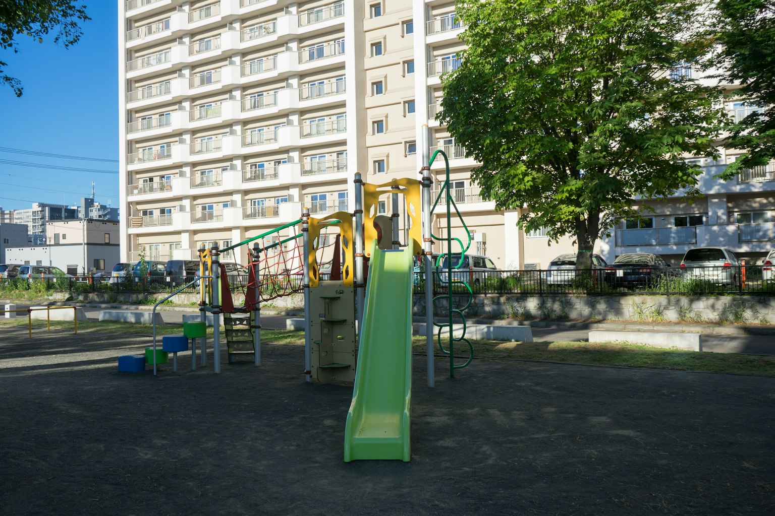 Parco giochi con uno scivolo verde e strutture di arrampicata di fronte a un edificio alto
