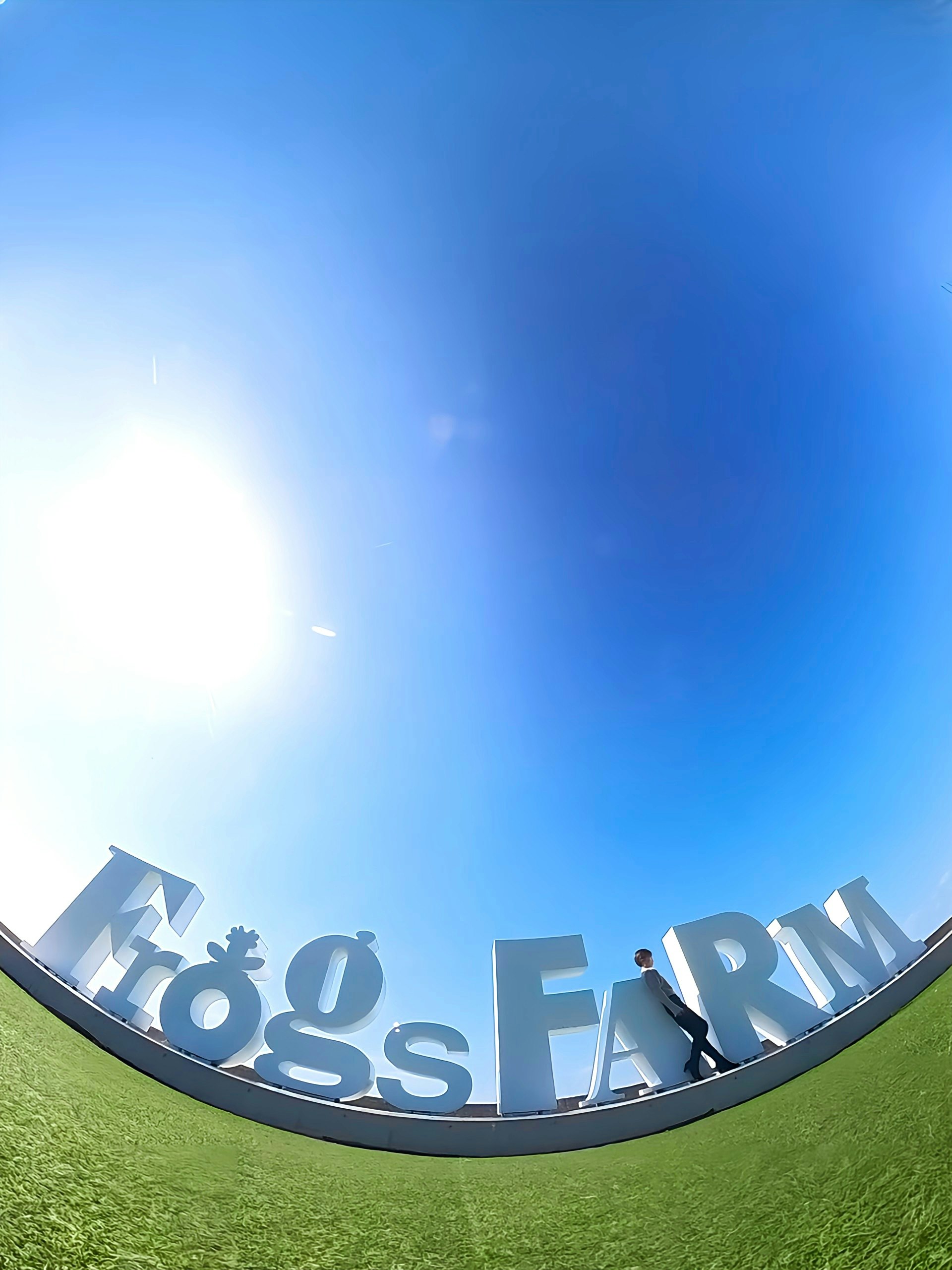 青空の下の芝生に設置された「HUGO BOSS FARM」サインの円形看板