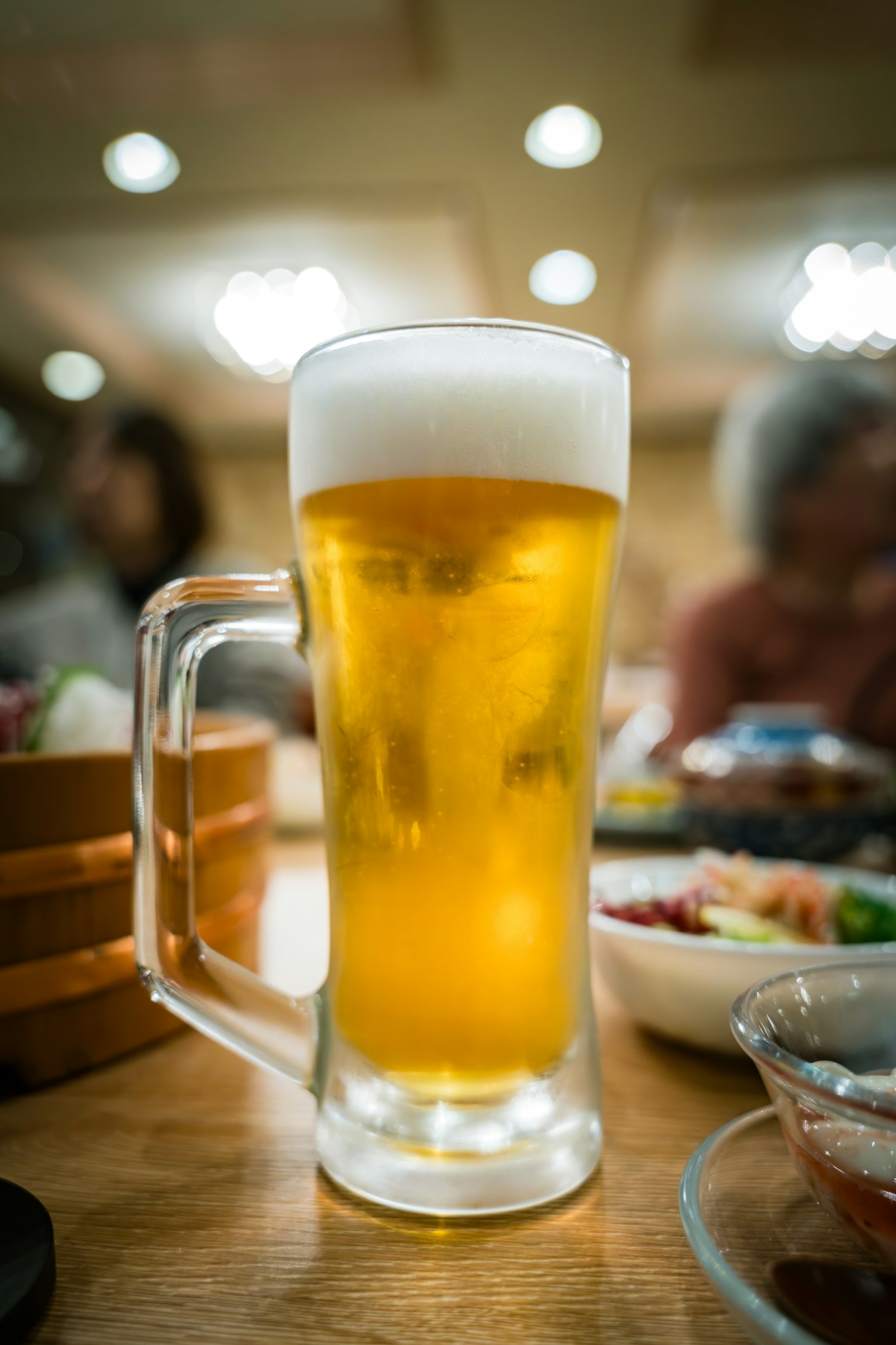 A clear glass of beer and various dishes on a table