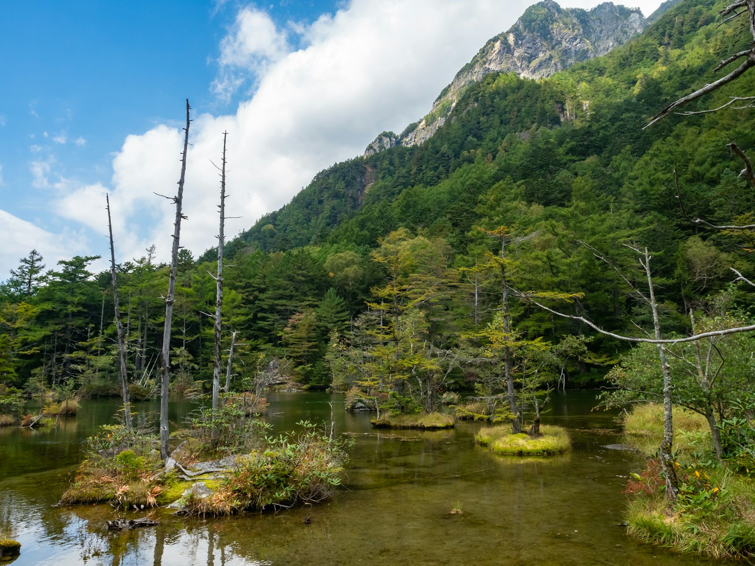Pemandangan indah gunung dan kolam dikelilingi oleh pepohonan hijau subur dan langit biru