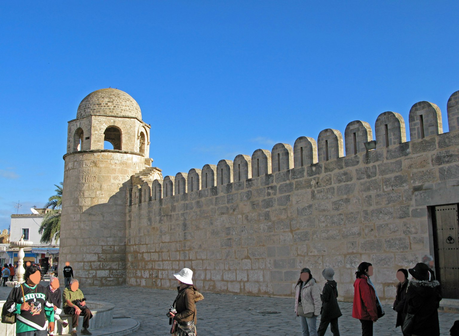 Mur en pierre avec une tour en dôme et des touristes
