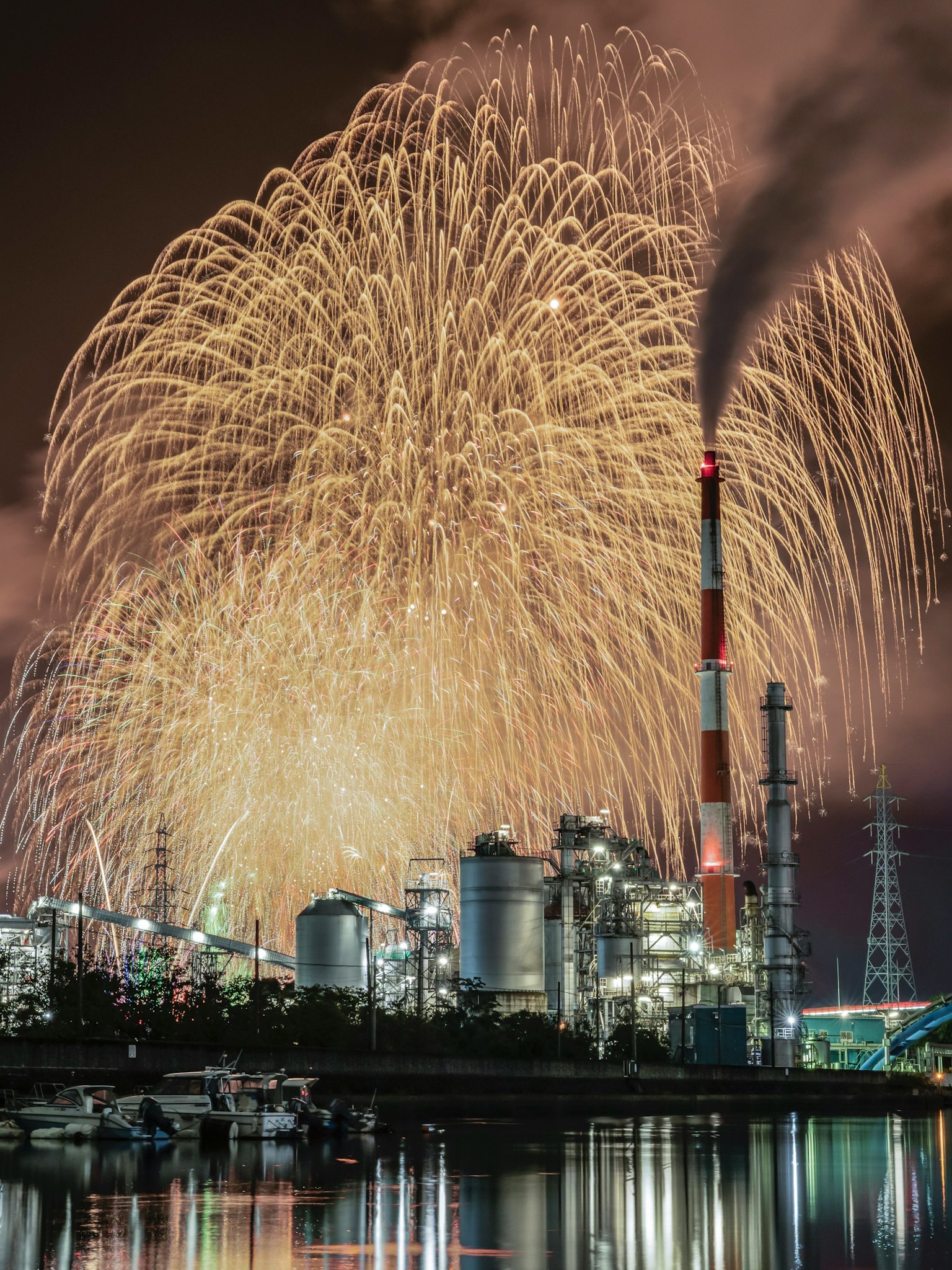 工場の煙突の背後に花火が上がる夜景