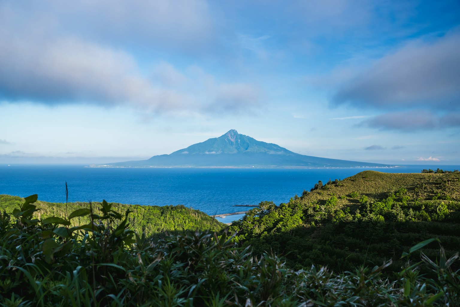 Mountain rising over blue sea and sky with green hills