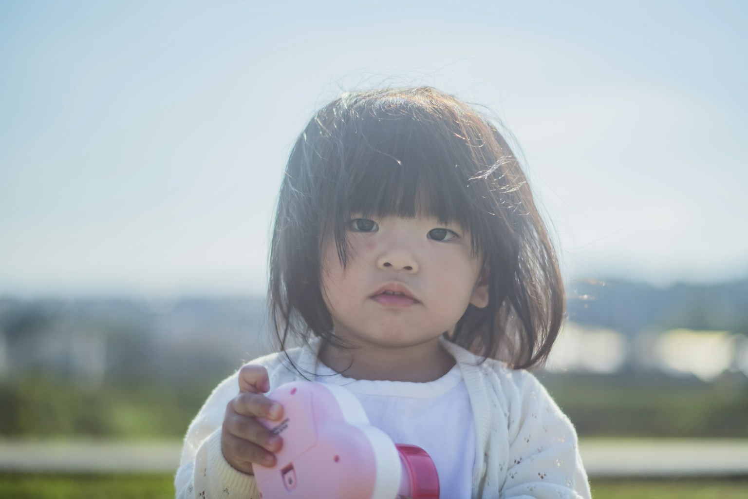 阳光明媚的日子里，一个小女孩手里拿着粉色玩具