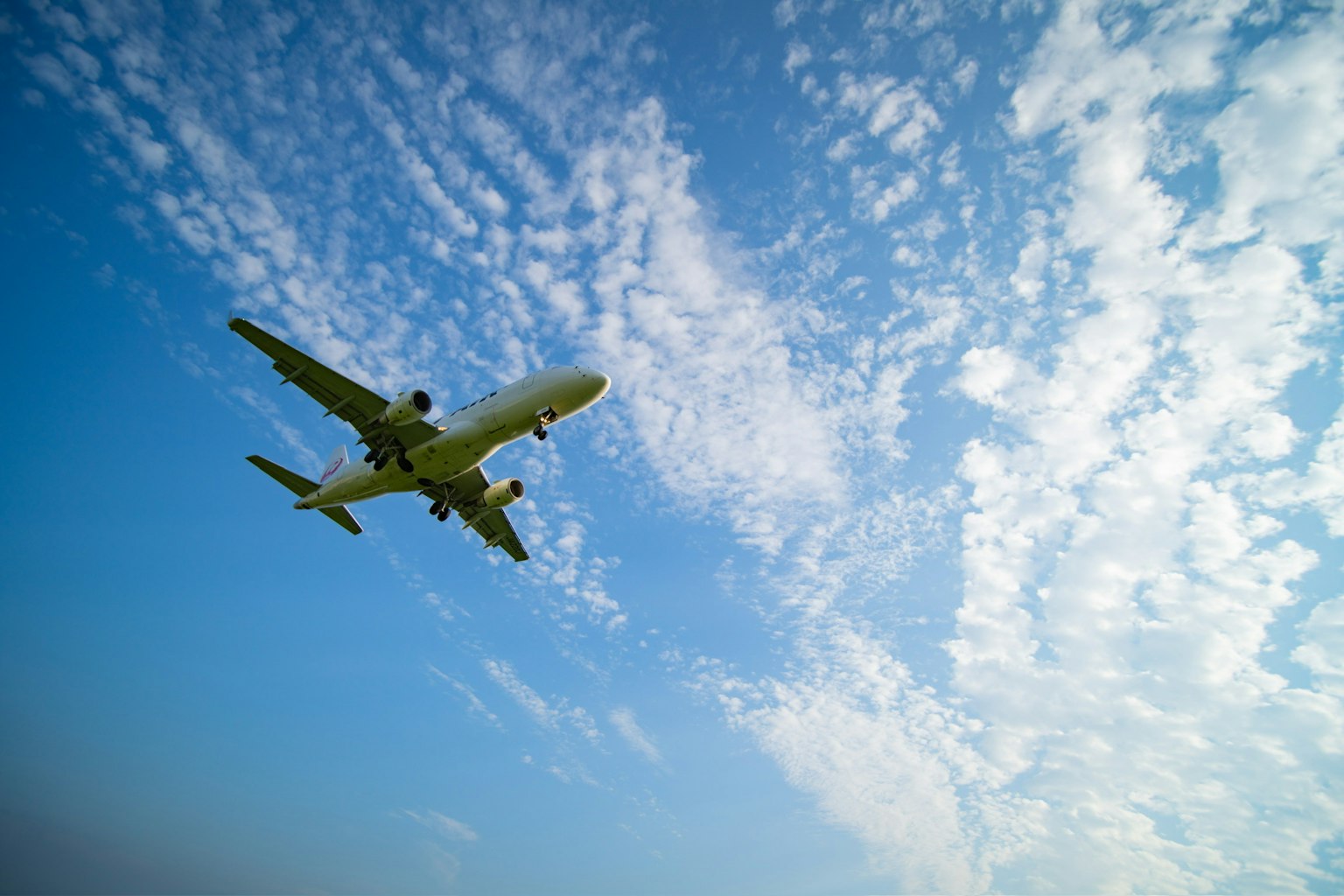 An airplane flying against a blue sky with white clouds