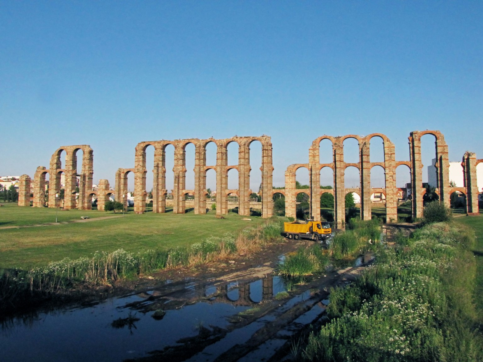 Reruntuhan aqueduct kuno di bawah langit biru dengan vegetasi di sekitarnya