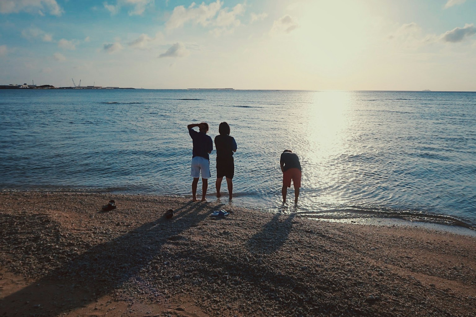 海辺で遊ぶ三人の子供たち夕日が反射する水面