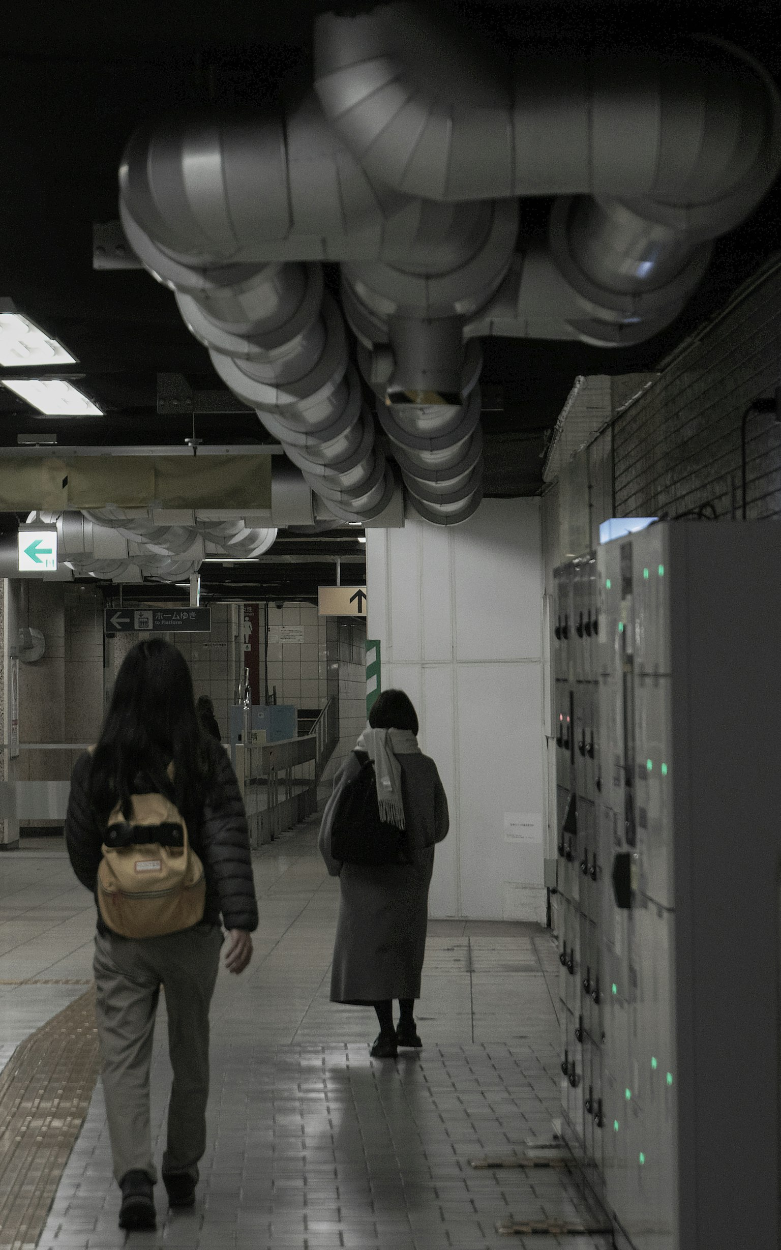 Due persone che camminano in un corridoio della metropolitana con tubi metallici sopra