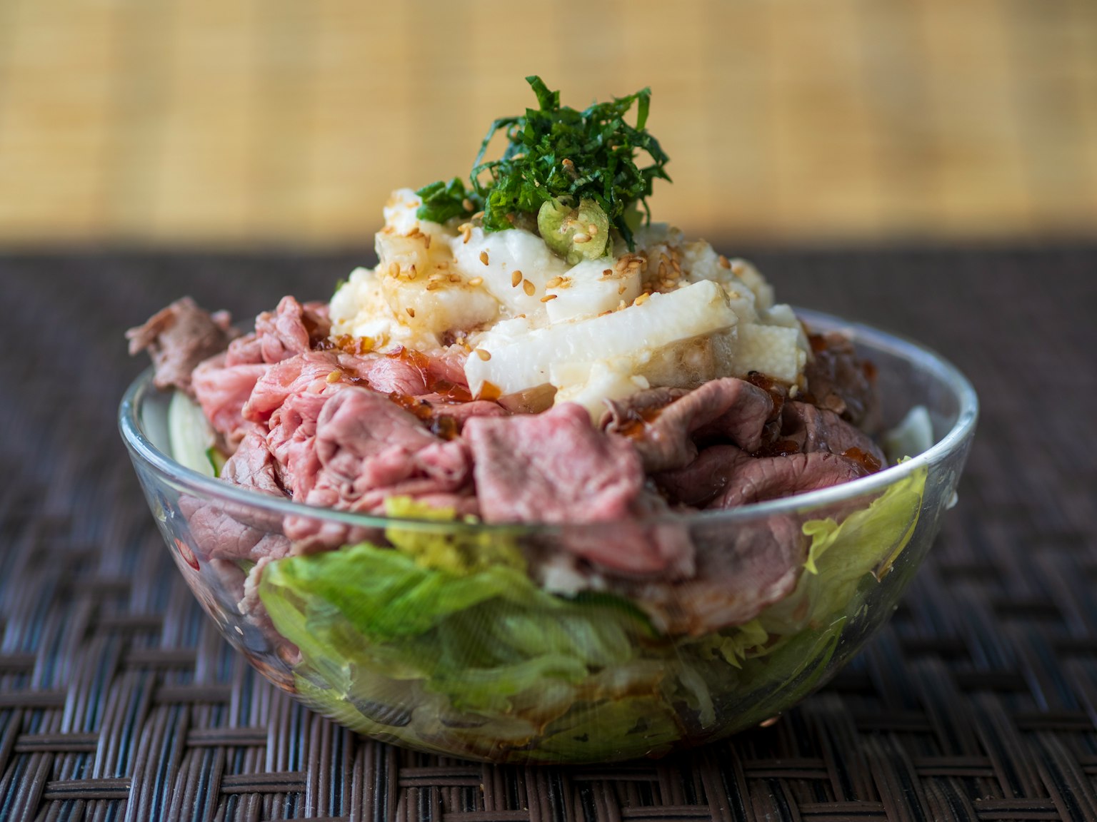 Sebuah mangkuk transparan yang diisi dengan salad daging panggang dan selada yang dihiasi dengan rempah hijau