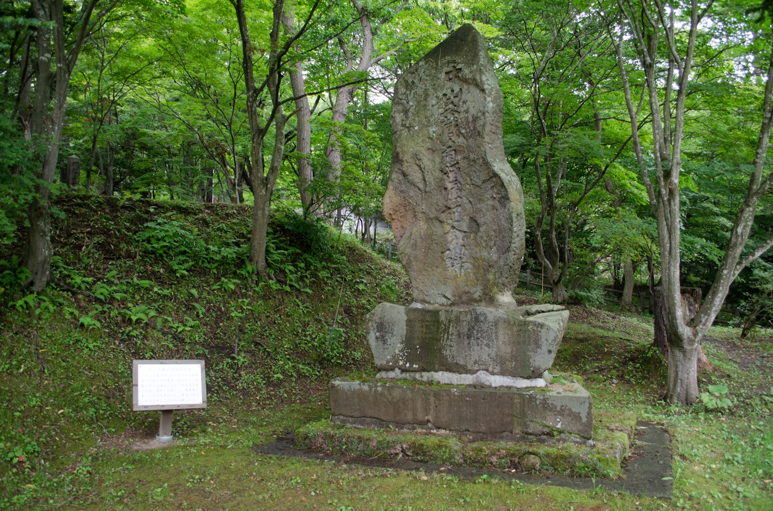 Grand monument en pierre entouré de verdure avec un panneau blanc devant