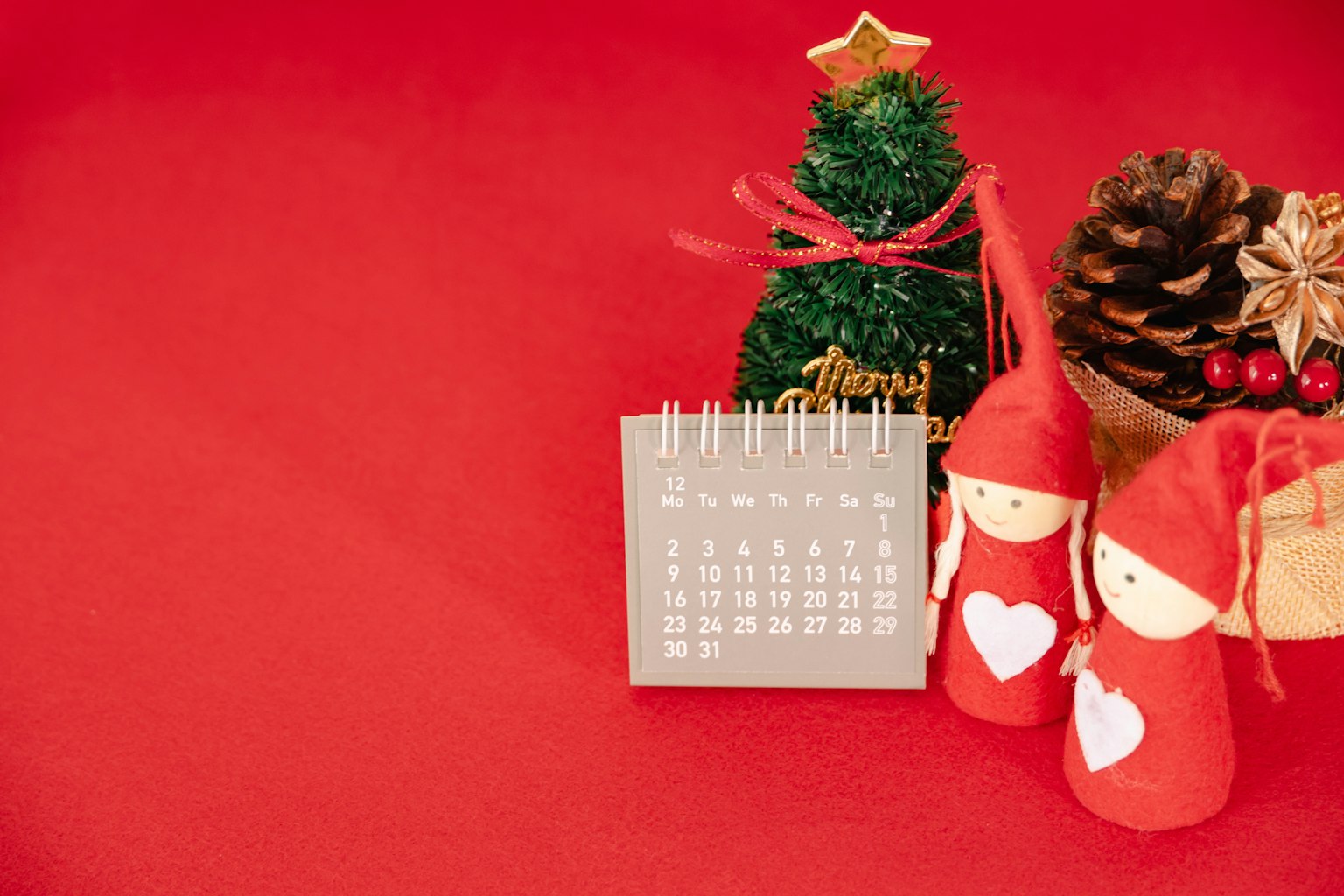 Pohon Natal dekoratif dan kalender dengan boneka di latar belakang merah