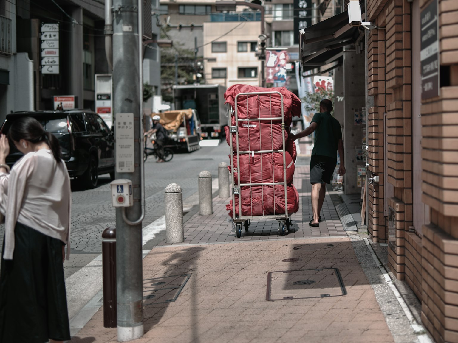 一個人在城市街道上推著紅色手推車，旁邊有行人