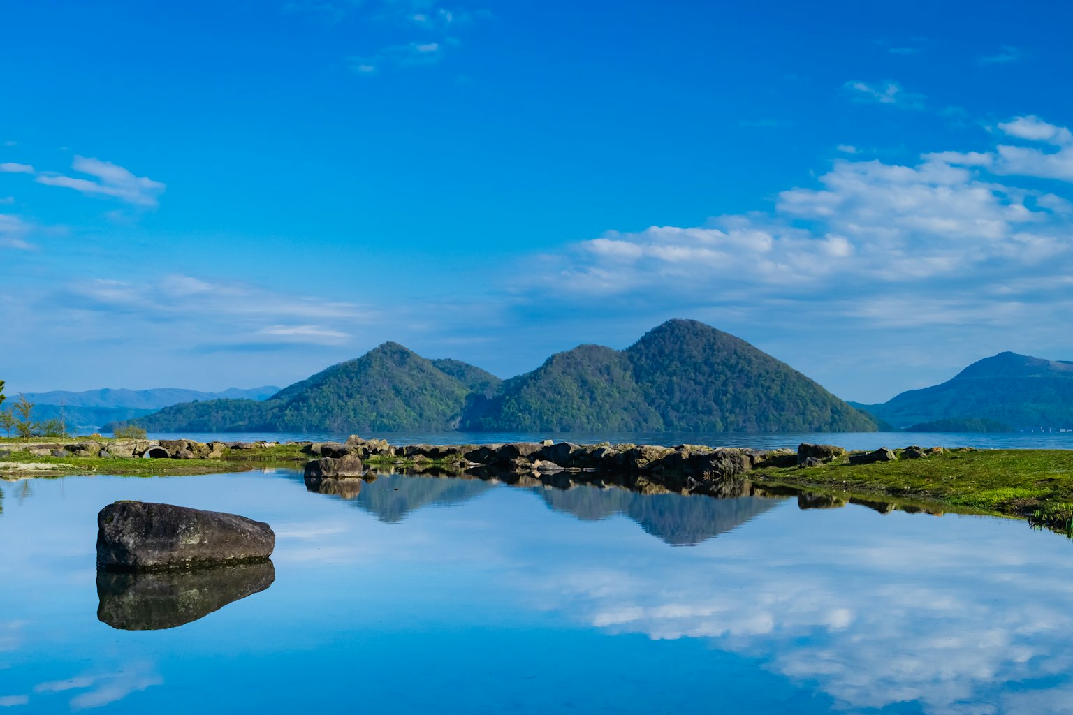 วิวทิวทัศน์ของทะเลสาบที่สะท้อนภูเขาใต้ท้องฟ้าสีฟ้า