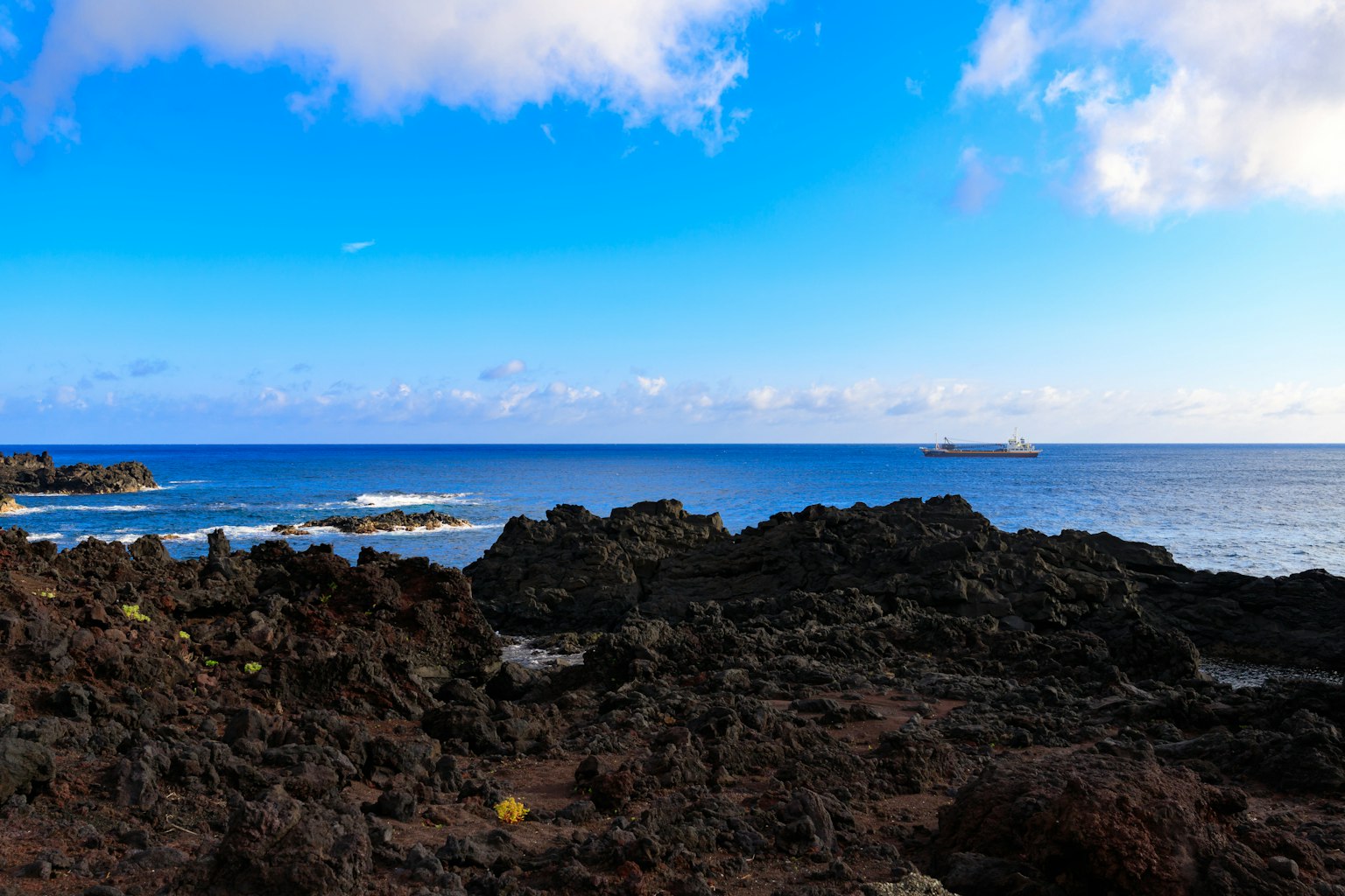 Paesaggio costiero con rocce nere sotto un cielo blu e l'oceano