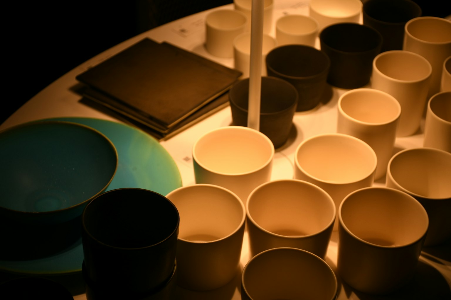 Disposición de tazas blancas y negras con un plato azul sobre una mesa iluminada por luz suave