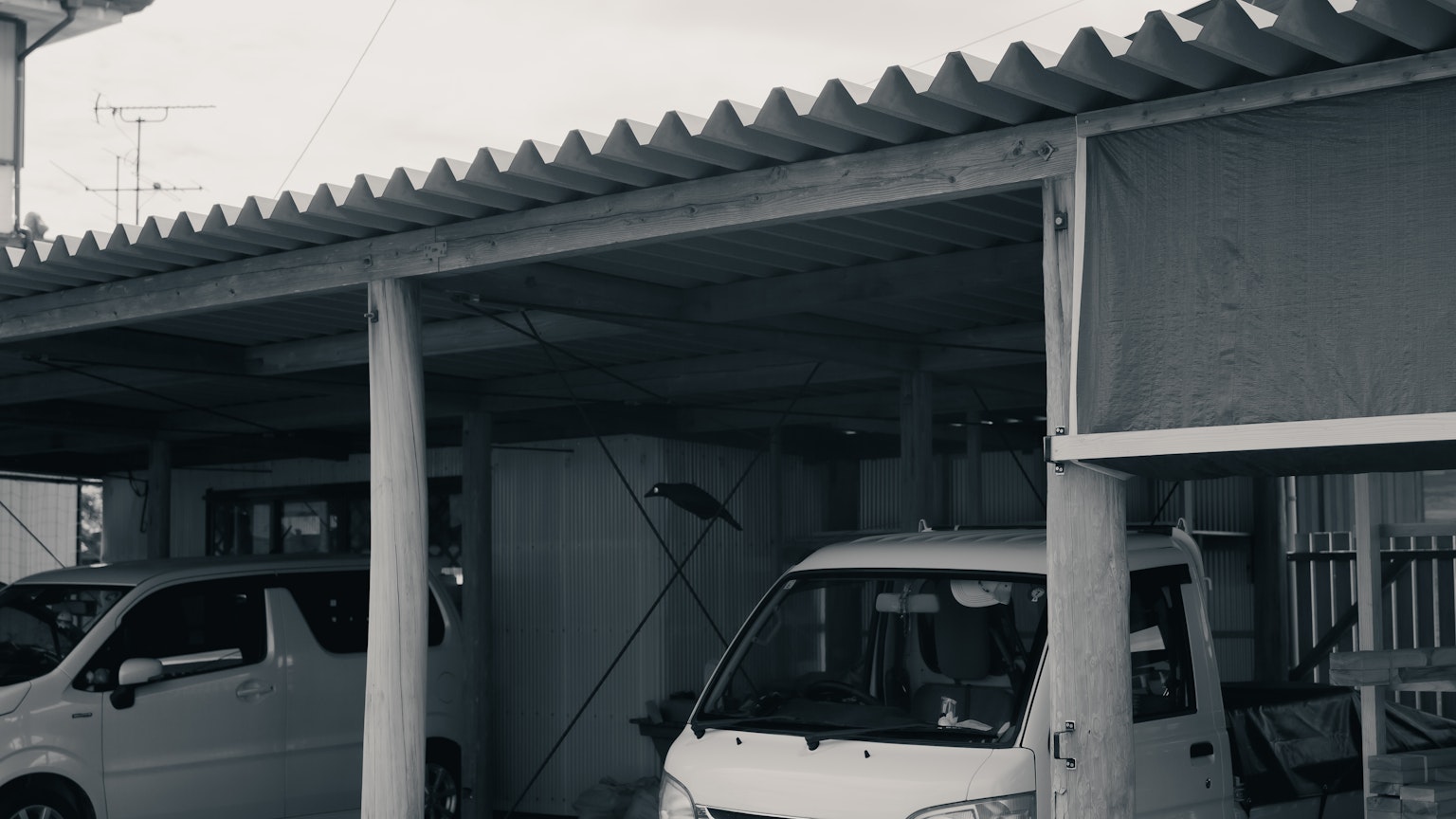 Black and white image of a parking area with two vehicles and a roof structure