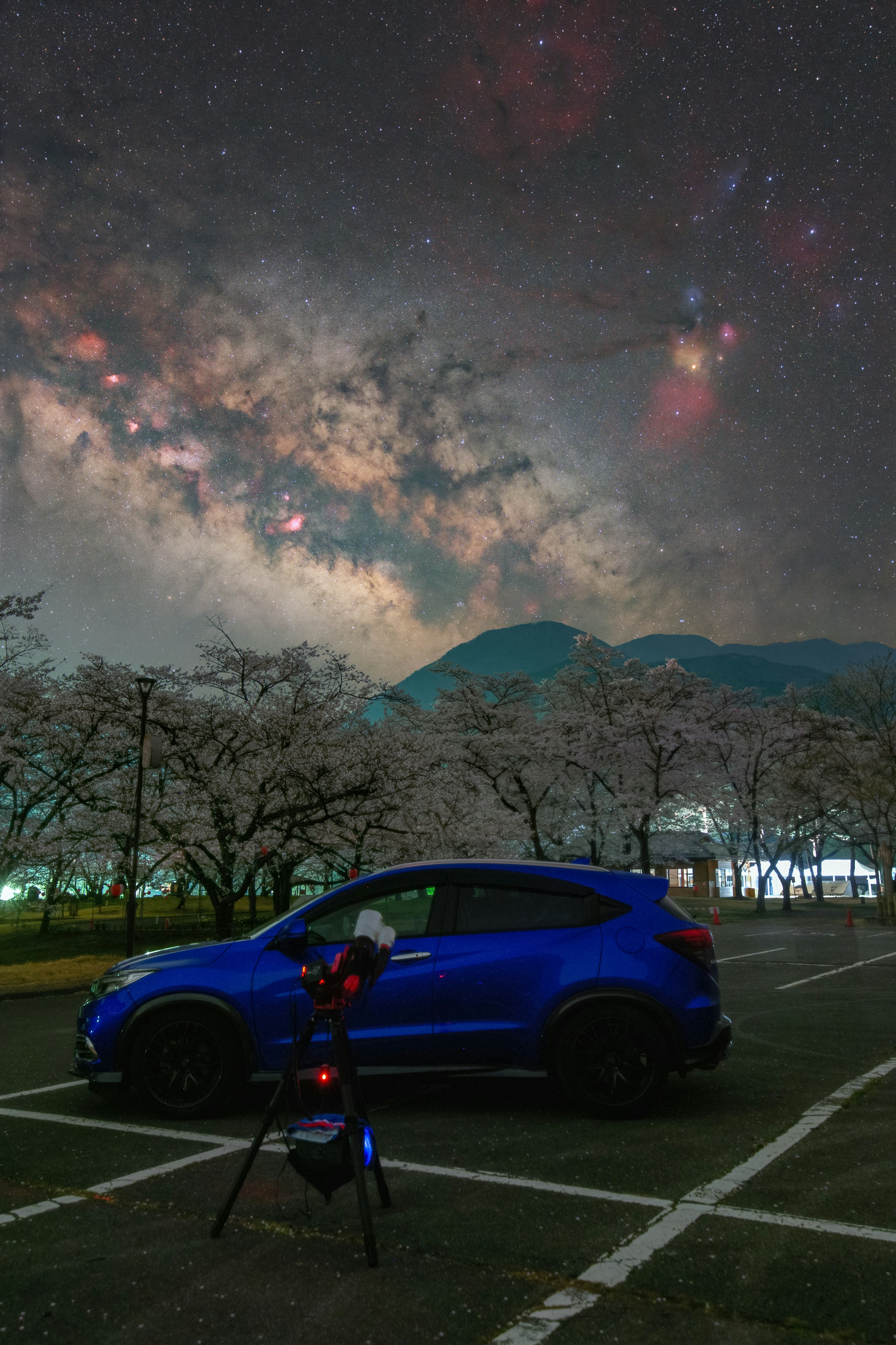 夜空の星と天の川、青い車が駐車場に停まる風景