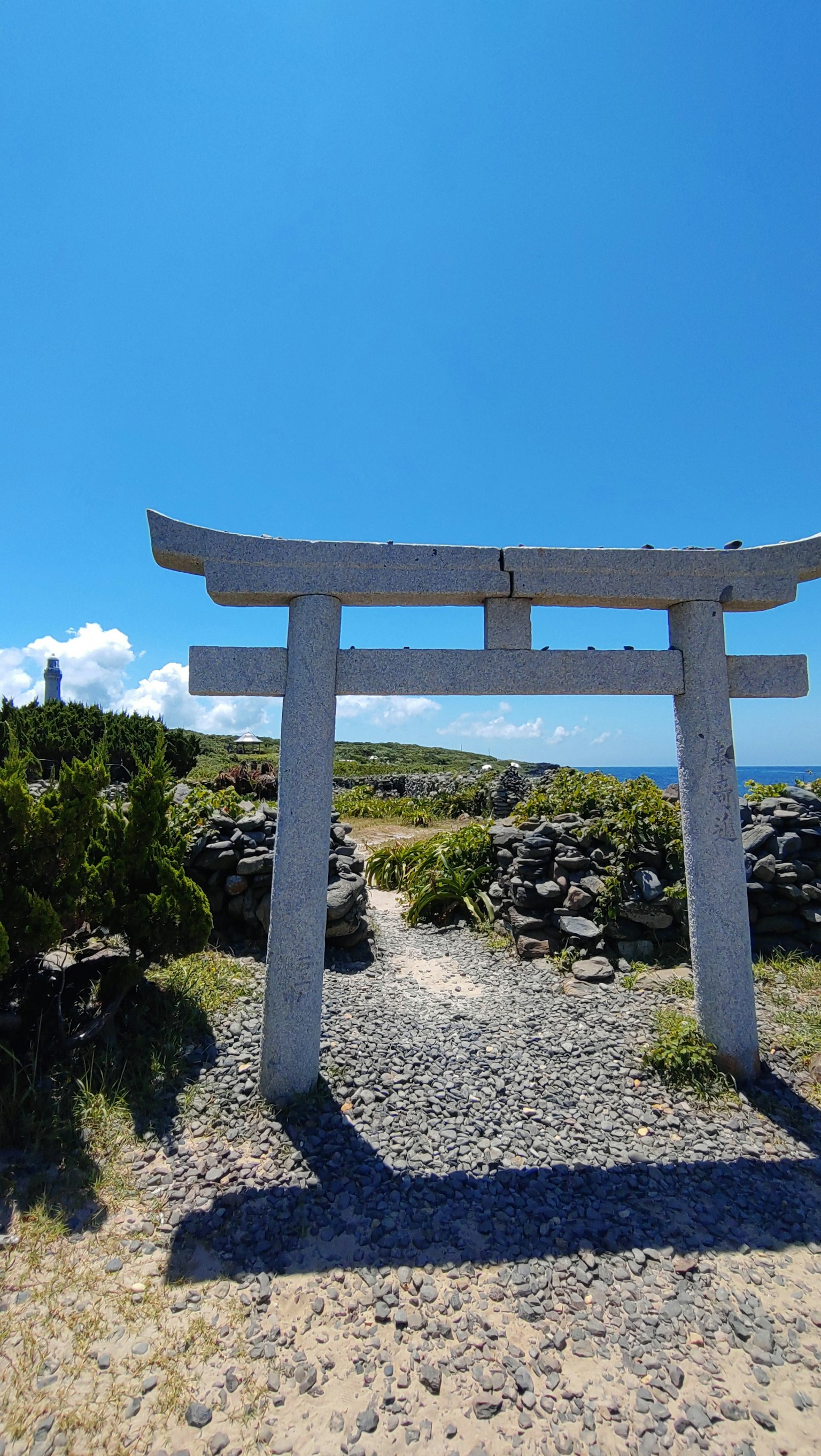 White torii gate under a blue sky with surrounding nature
