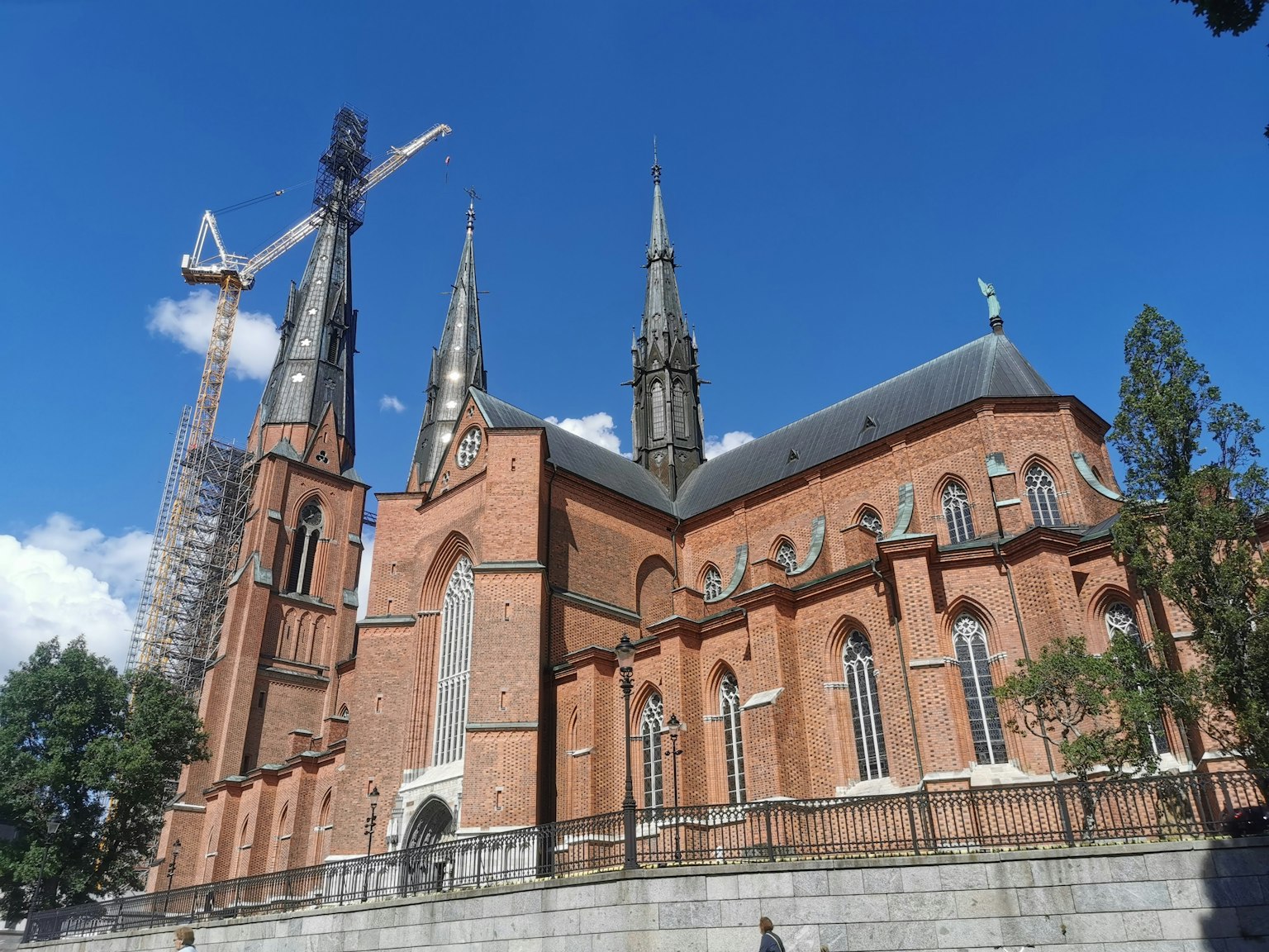 Side view of a red brick church with tall spires and a construction crane