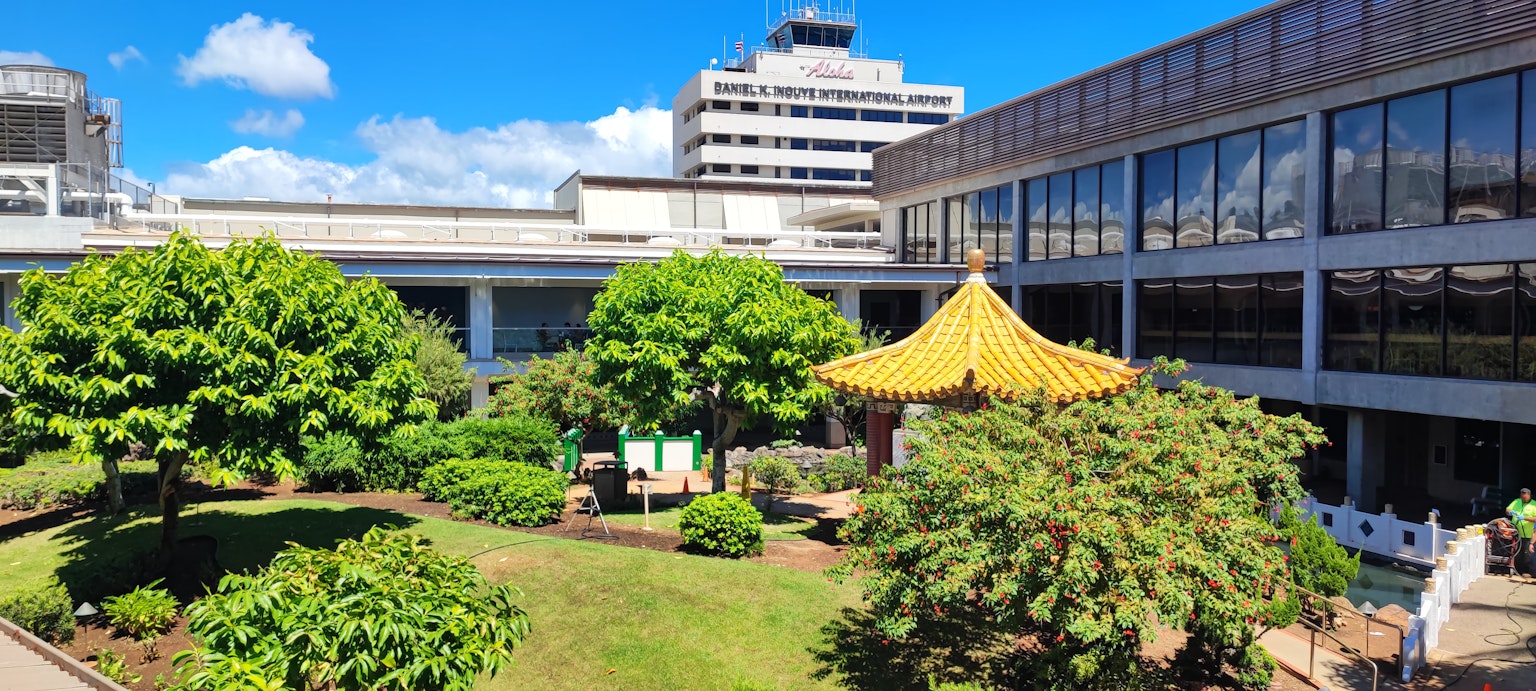 Jardín exuberante con un pabellón de techo amarillo y edificios modernos al fondo