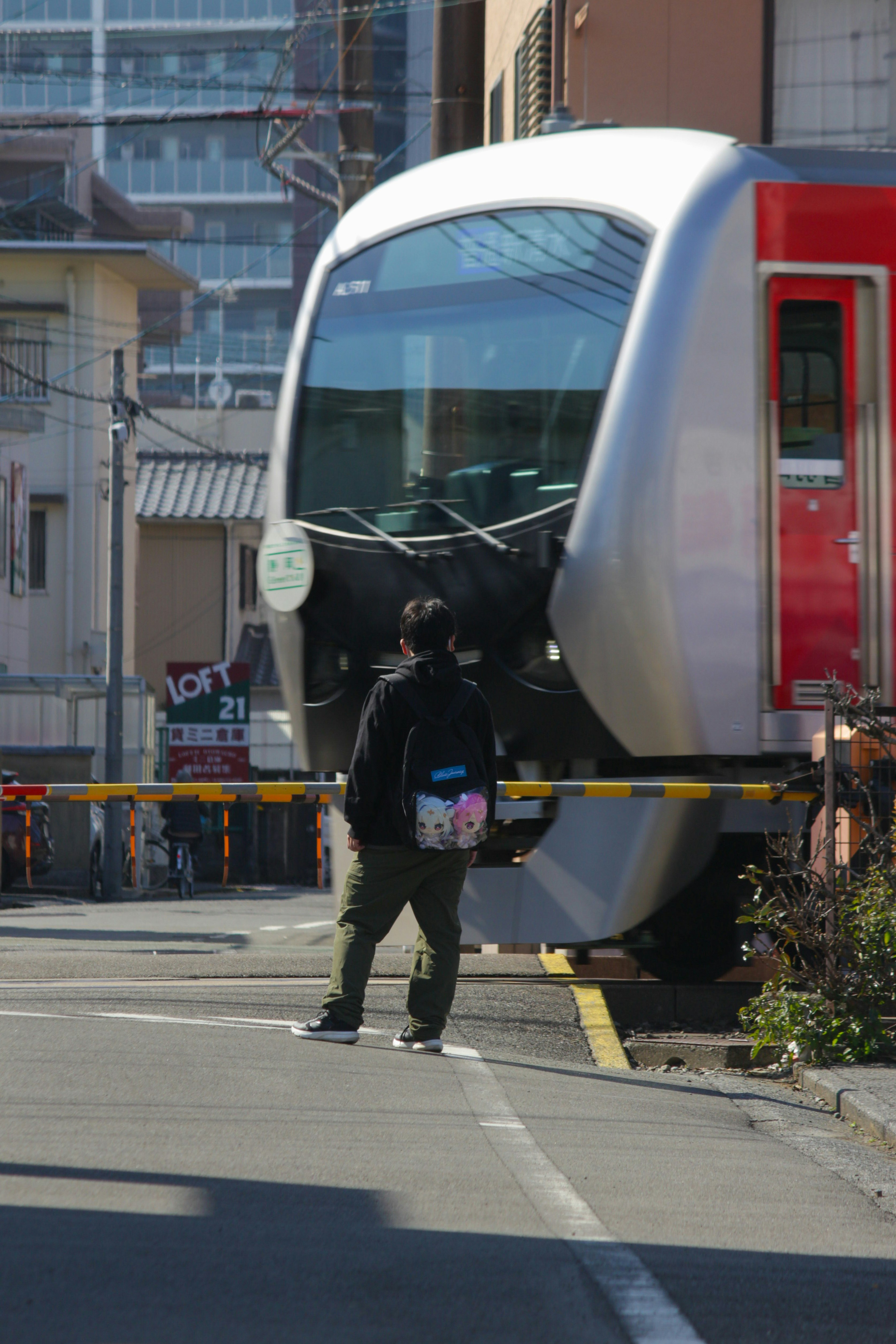 踏切で停車する電車と人のいる駅前の街並み