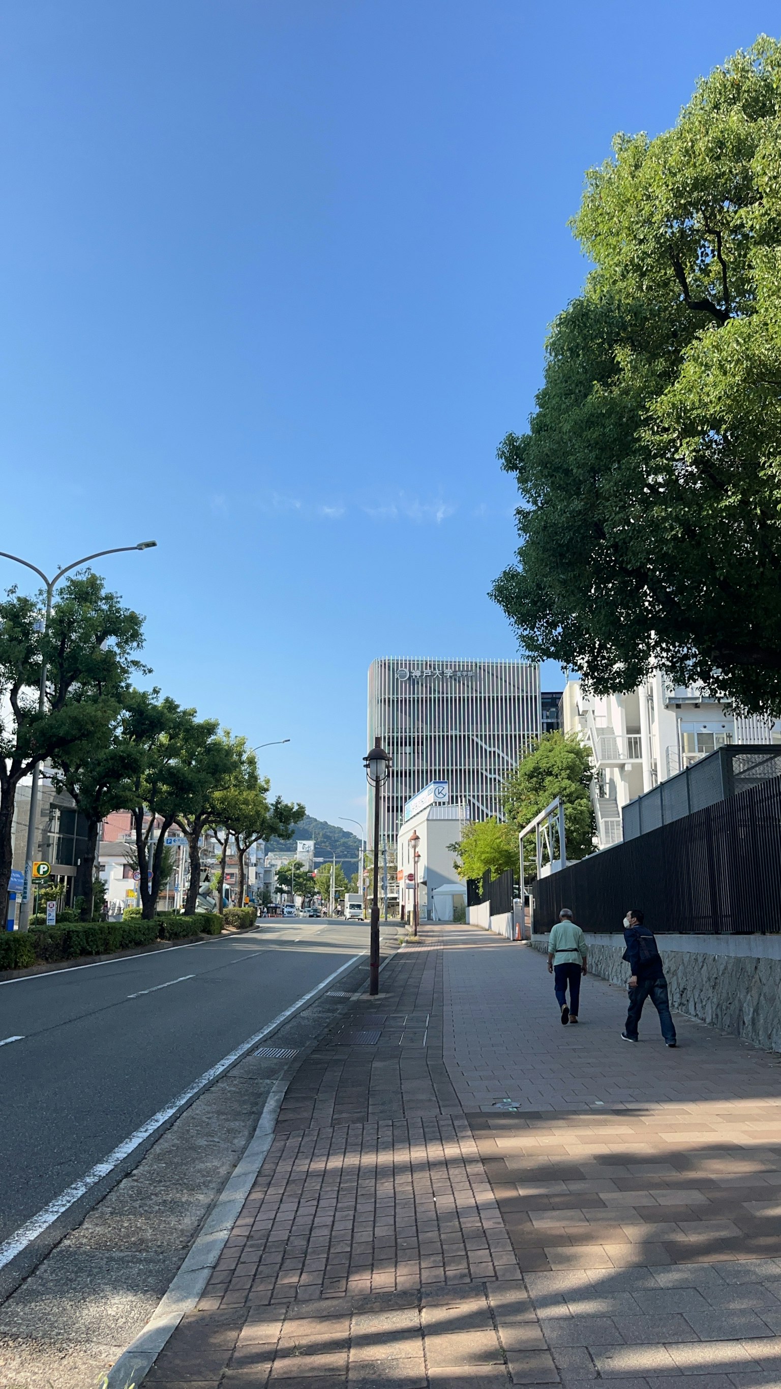 Due pedoni che camminano su una strada tranquilla sotto un cielo azzurro con edifici moderni
