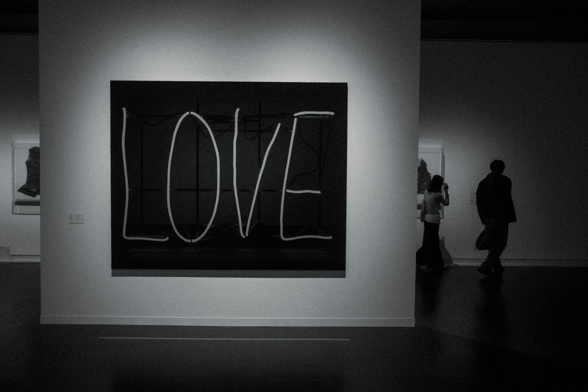 tác phẩm tường phong cách neon “LOVE” trong phòng triển lãm với bóng người