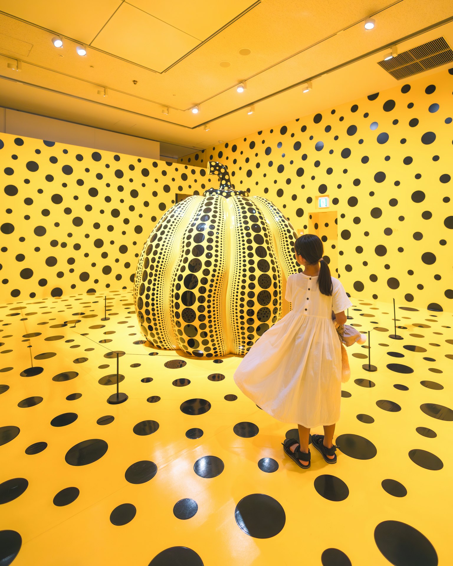 Child in a polka dot room with a large yellow pumpkin sculpture