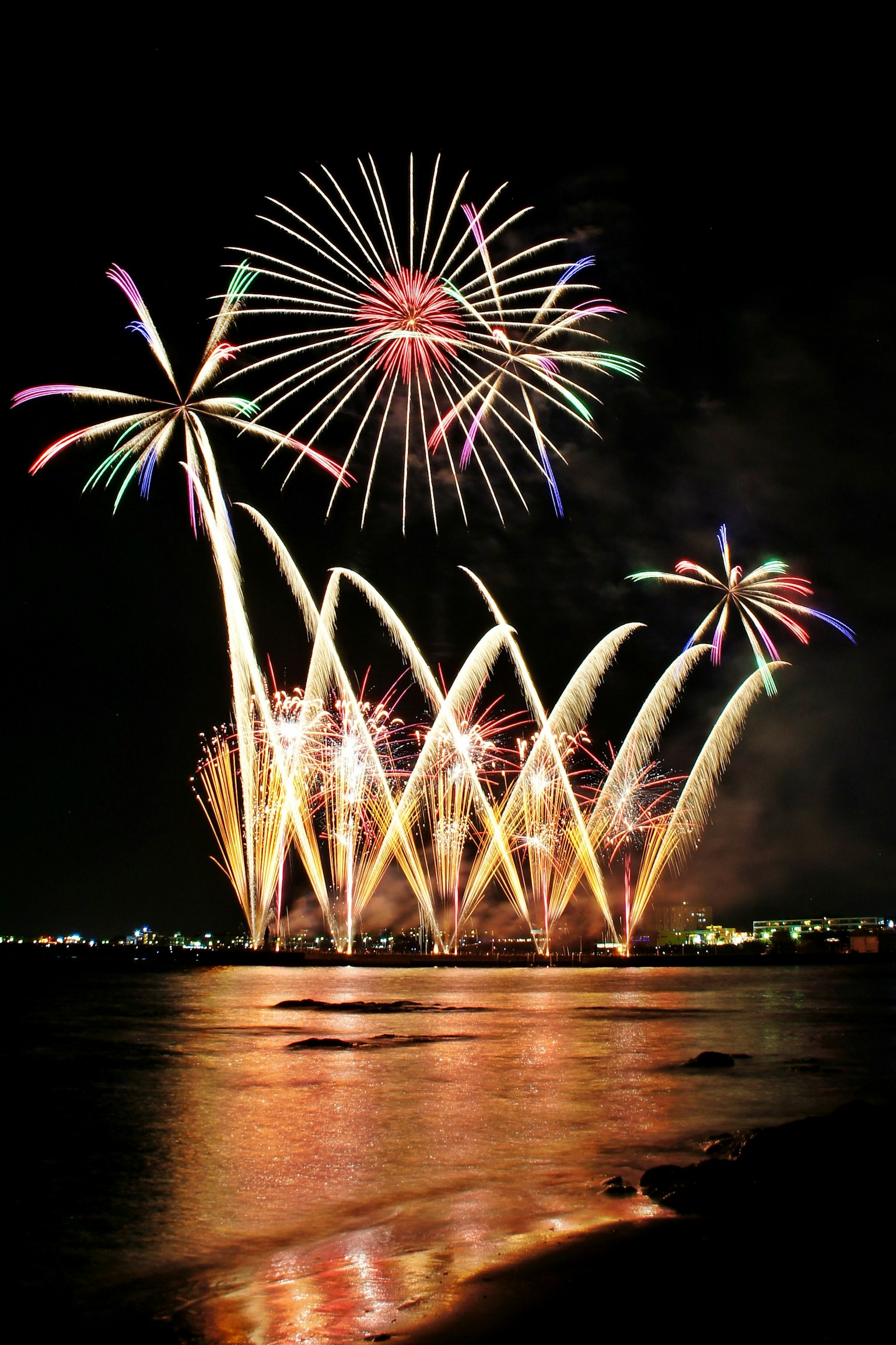 Fuochi d'artificio colorati che esplodono nel cielo notturno riflettendosi sulla superficie dell'oceano