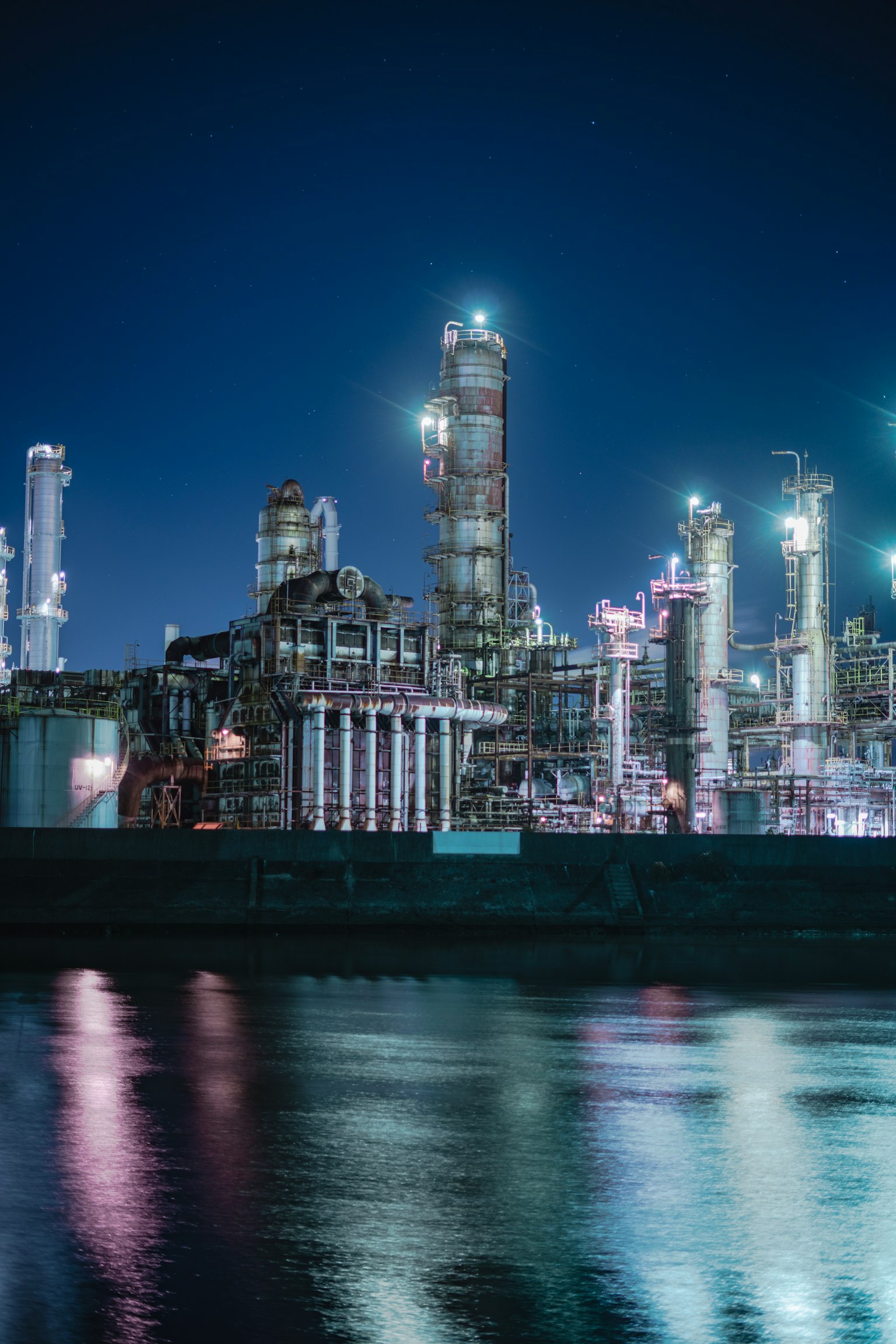 Industrielle Anlage bei Nacht beleuchtet, spiegelt sich im Wasser
