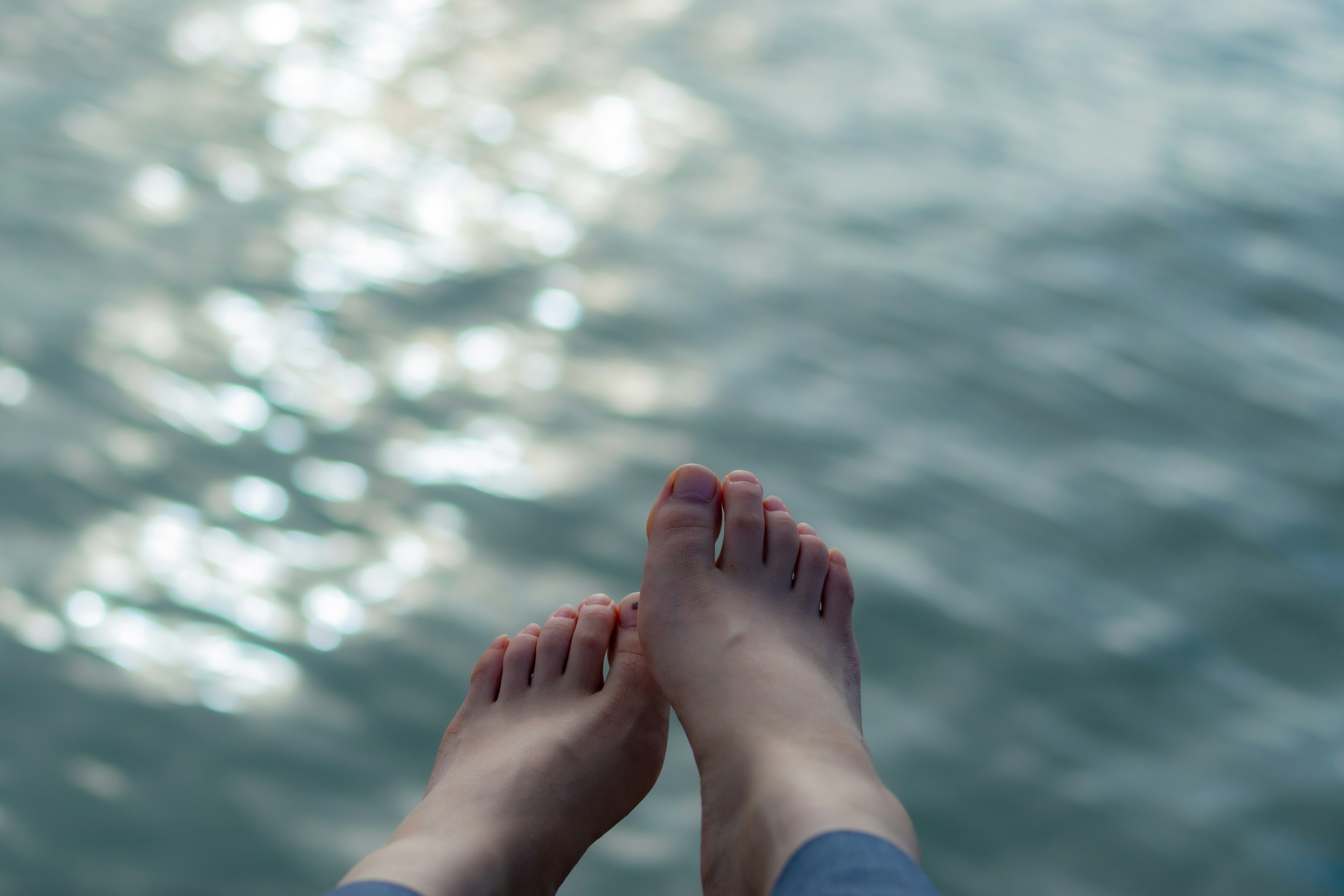 波打ち際で足を水に浸す人の足元
