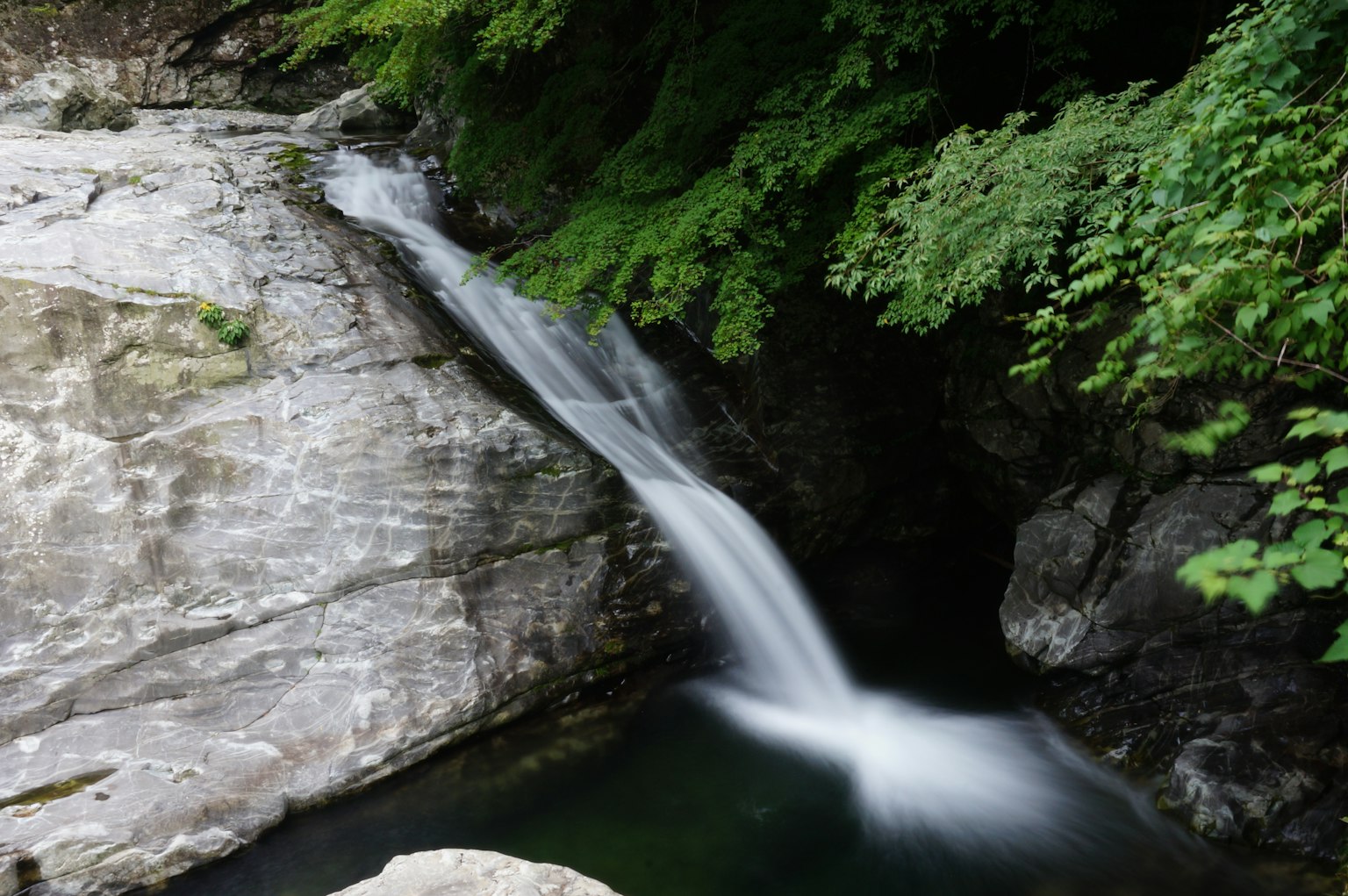 Air terjun yang indah mengalir di atas batu halus dikelilingi oleh dedaunan yang rimbun