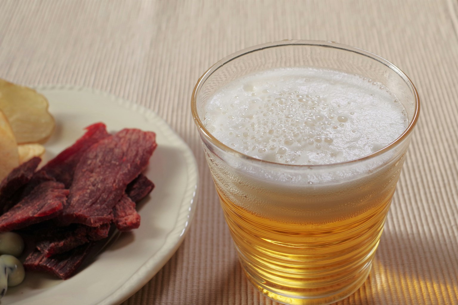 Un verre de bière à côté d'une assiette de collations comprenant des chips et de la viande séchée