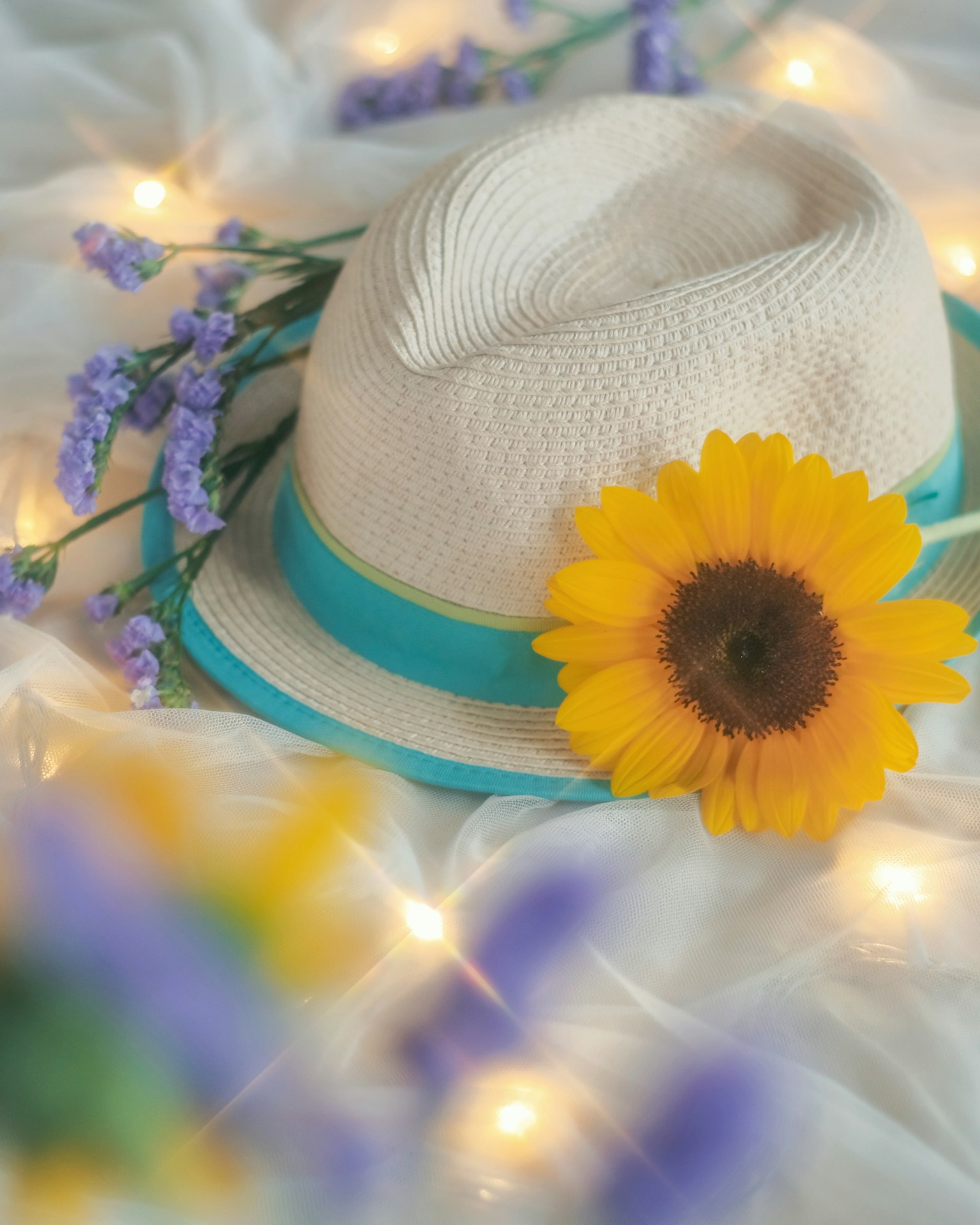 A white hat adorned with a sunflower and lavender flowers in a soft setting