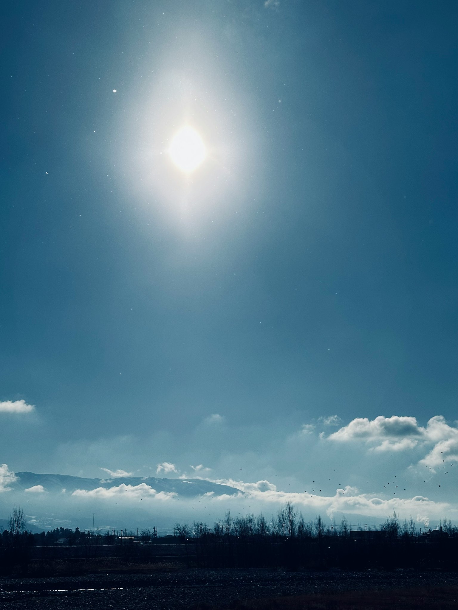 ดวงอาทิตย์สว่างในท้องฟ้าสีฟ้ากับเมฆและภูเขา