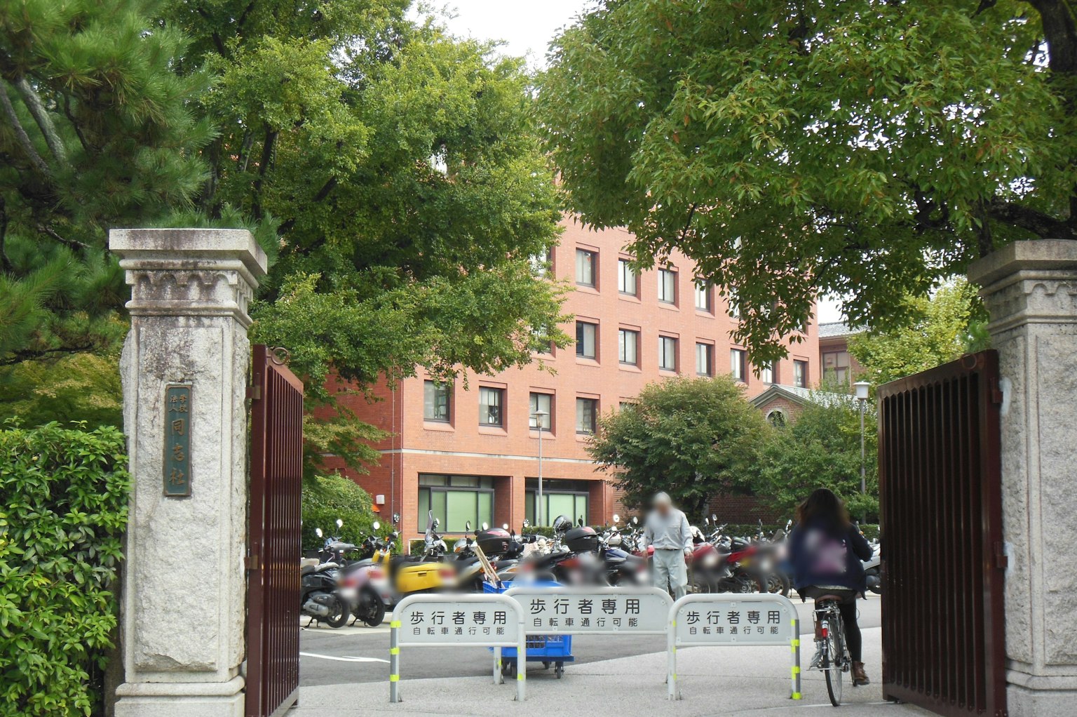 Entrata con pilastri di pietra che porta a un edificio in mattoni rossi circondato da alberi
