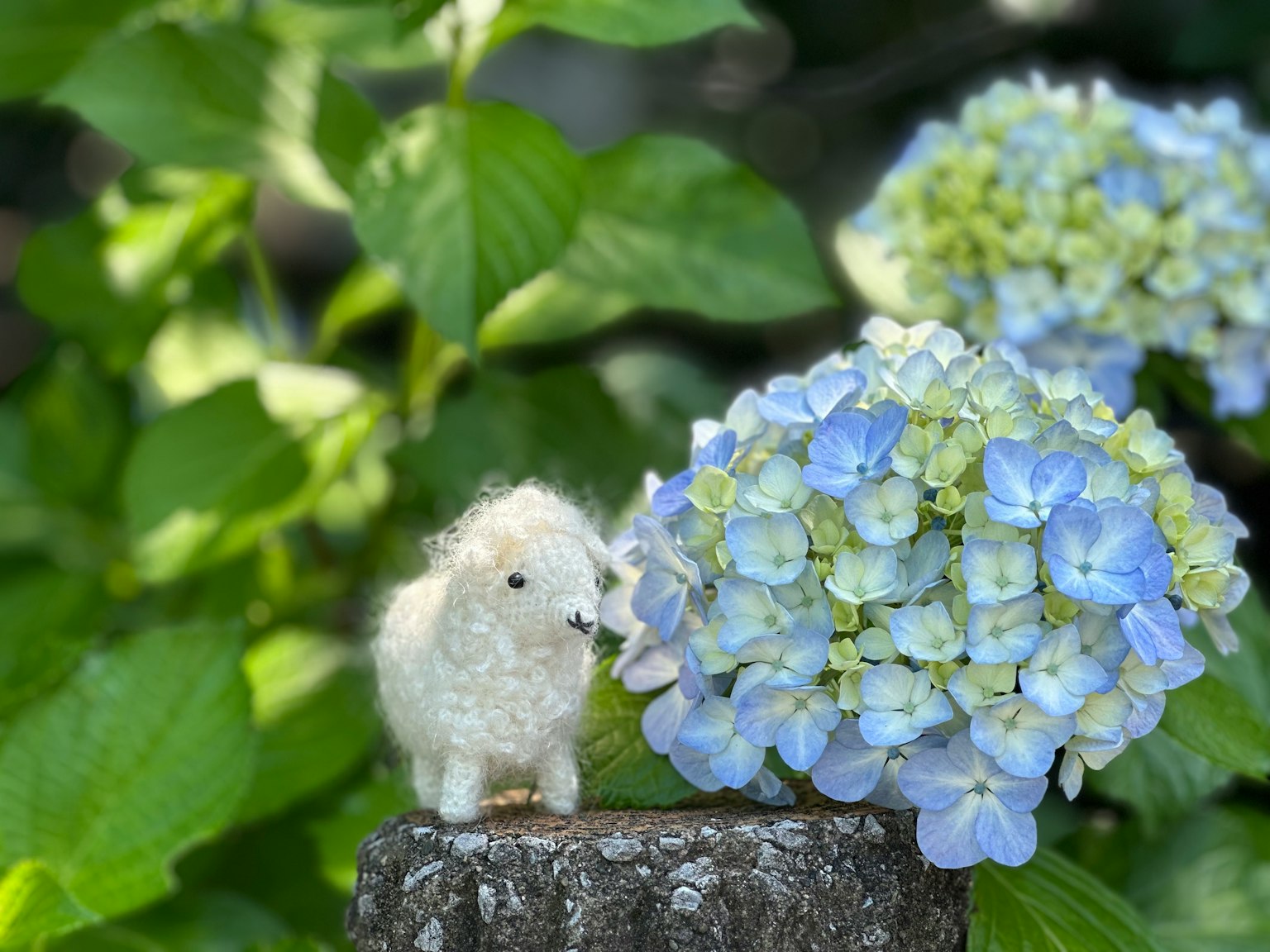 Una figurina di pecora bianca accanto a fiori di ortensia blu in un giardino
