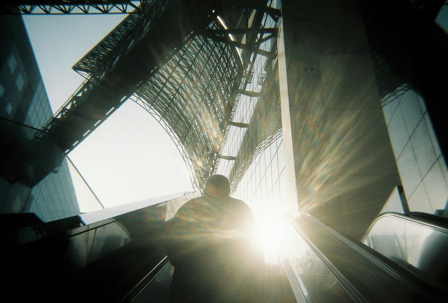 Person ascending an escalator with bright light in a modern architectural space