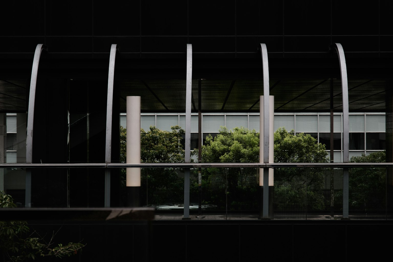 Balcone in vetro di un edificio nero con alberi verdi e pilastri verticali