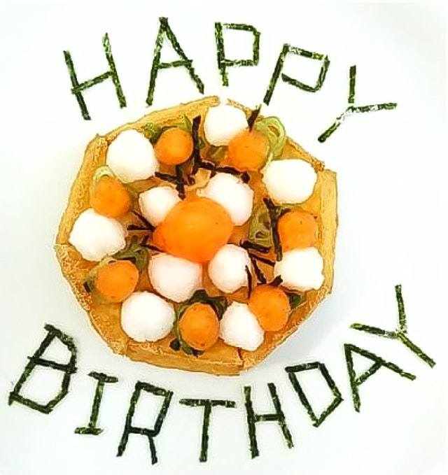 เค้กวันเกิดที่ตกแต่งด้วยผลไม้และครีม พร้อมคำว่า 'HAPPY BIRTHDAY' ทำจากใบเขียว