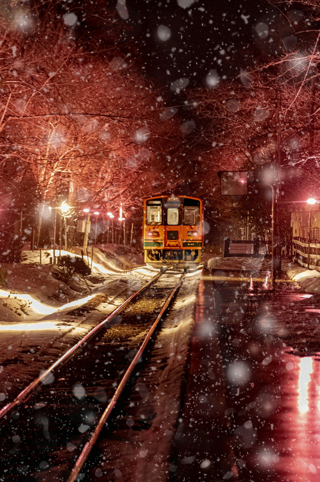 snowy night railway tracks with a passing train at a station