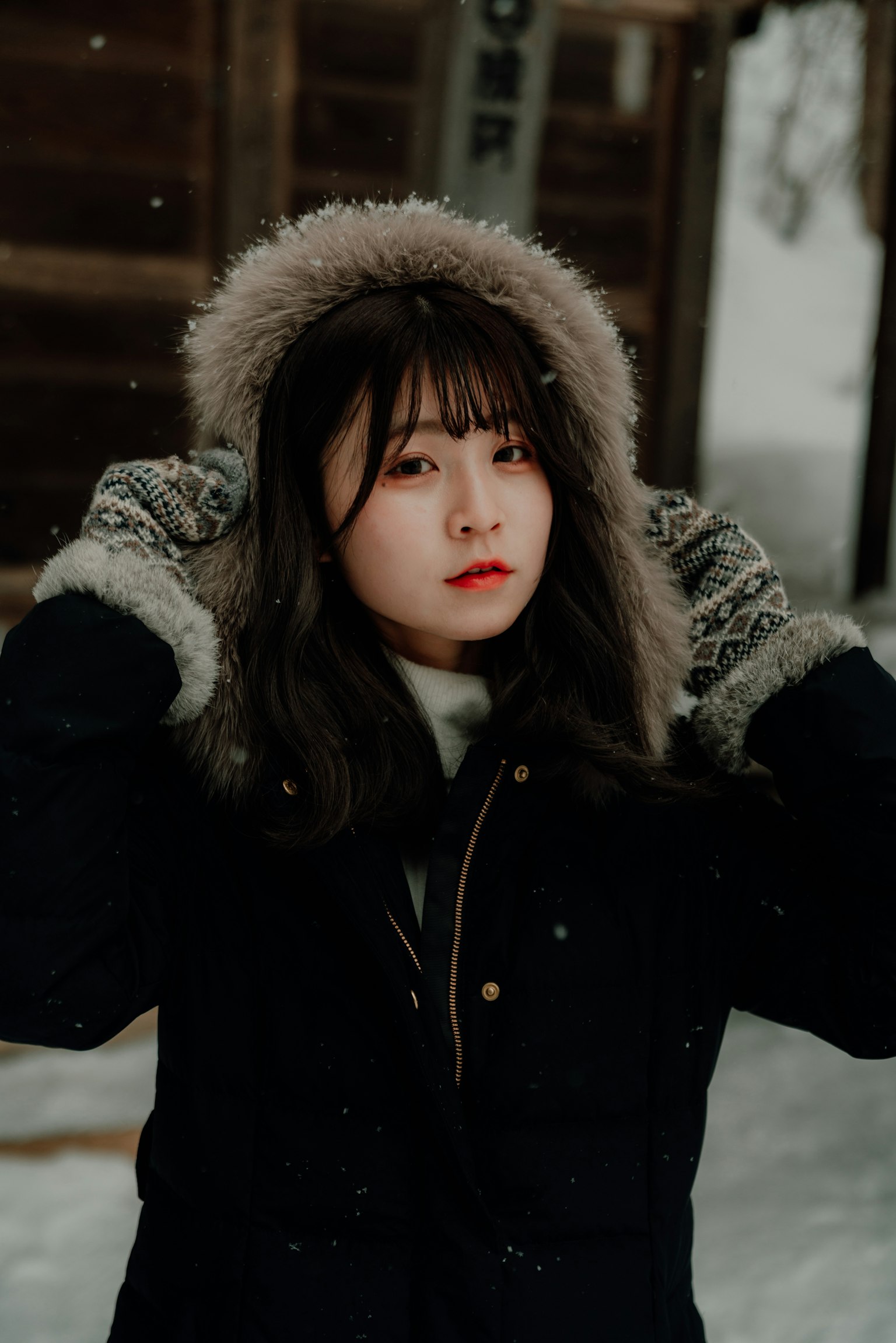 Retrato de una mujer en la nieve usando guantes y un abrigo negro con capucha de piel
