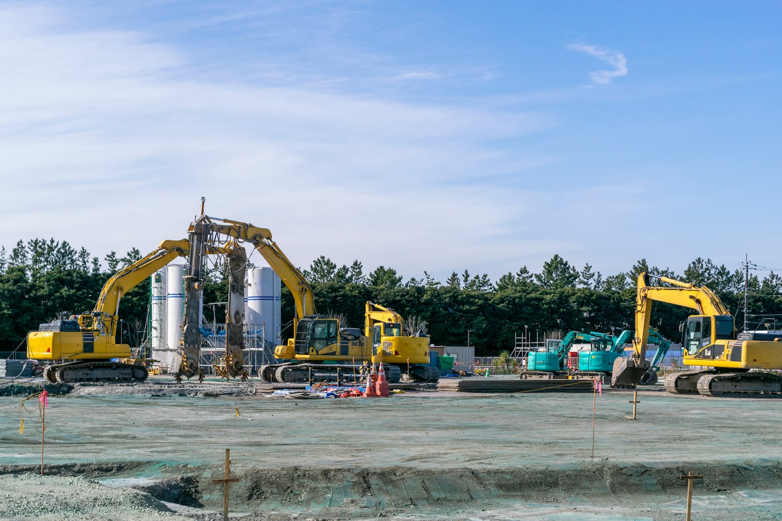 Construction site with yellow excavators and large silver tanks