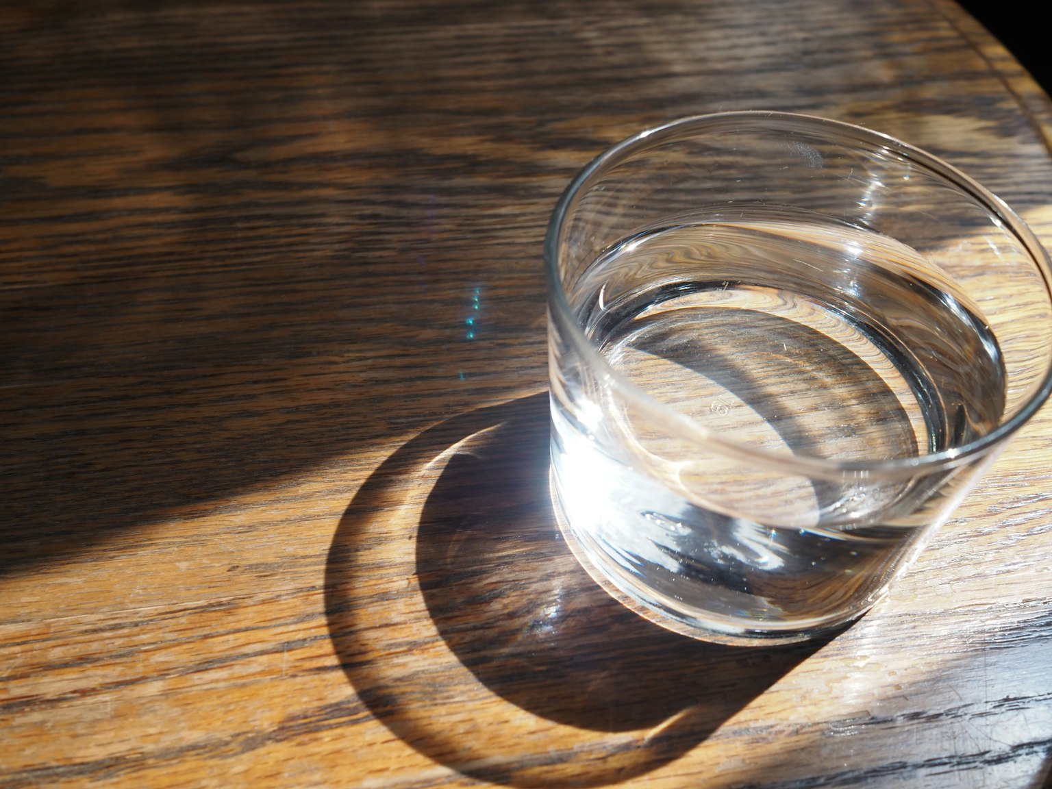 一个装有水的透明玻璃杯放在木桌上,投下阴影
