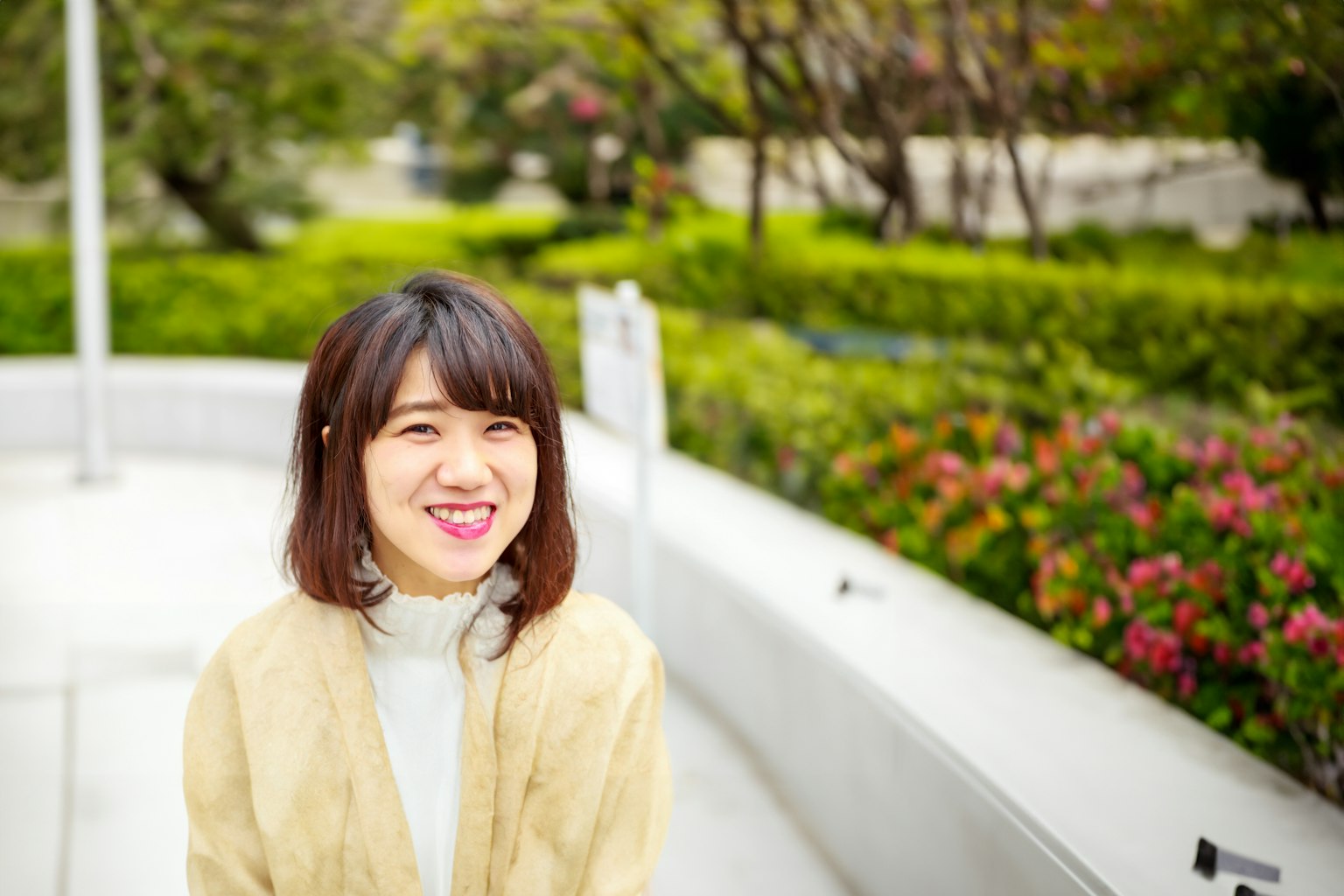 공원에서 미소 짓고 있는 여성의 초상 배경에 녹지와 꽃이 보임