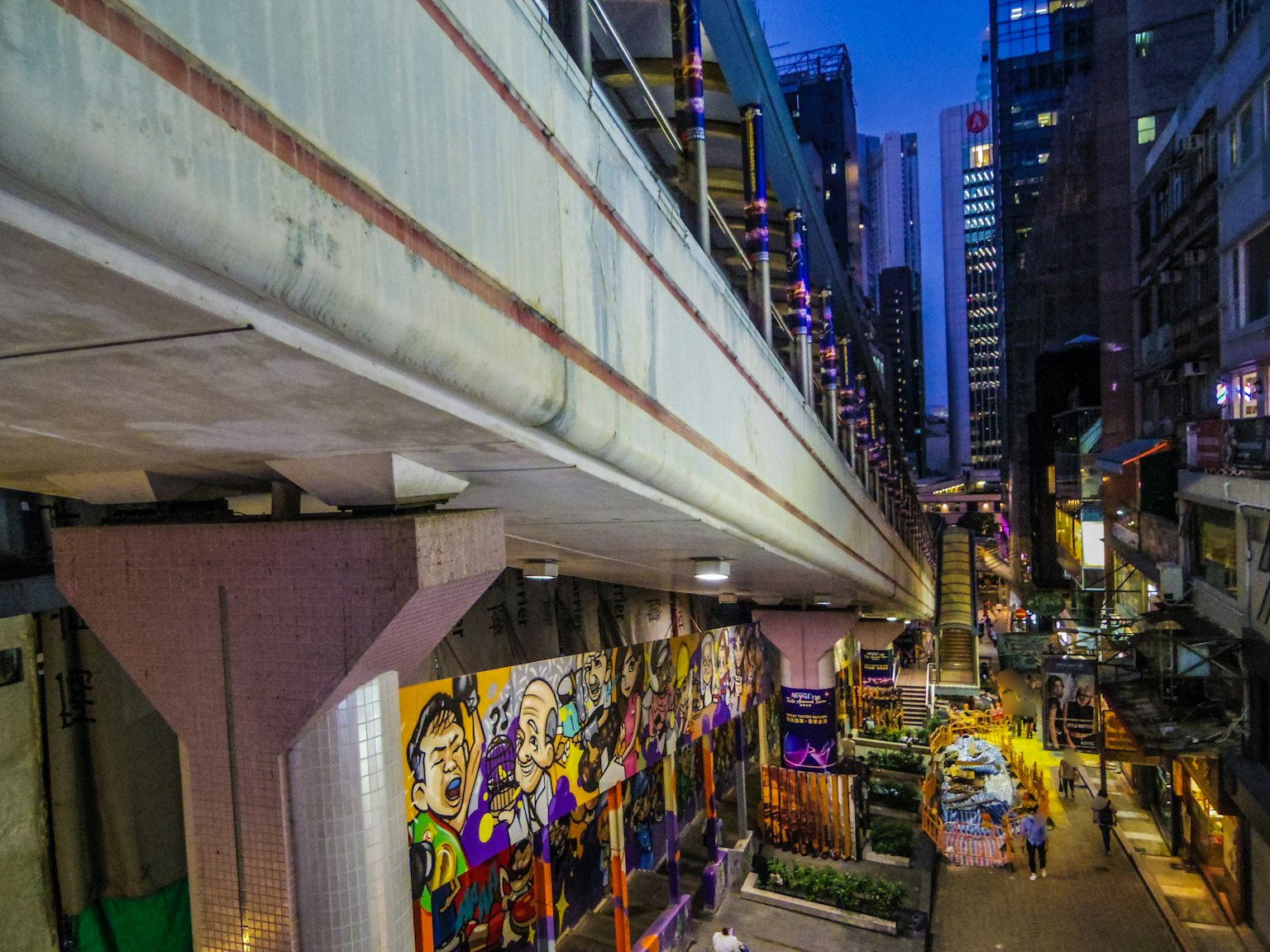 Night view of a city with tall buildings and colorful graffiti under an elevated walkway