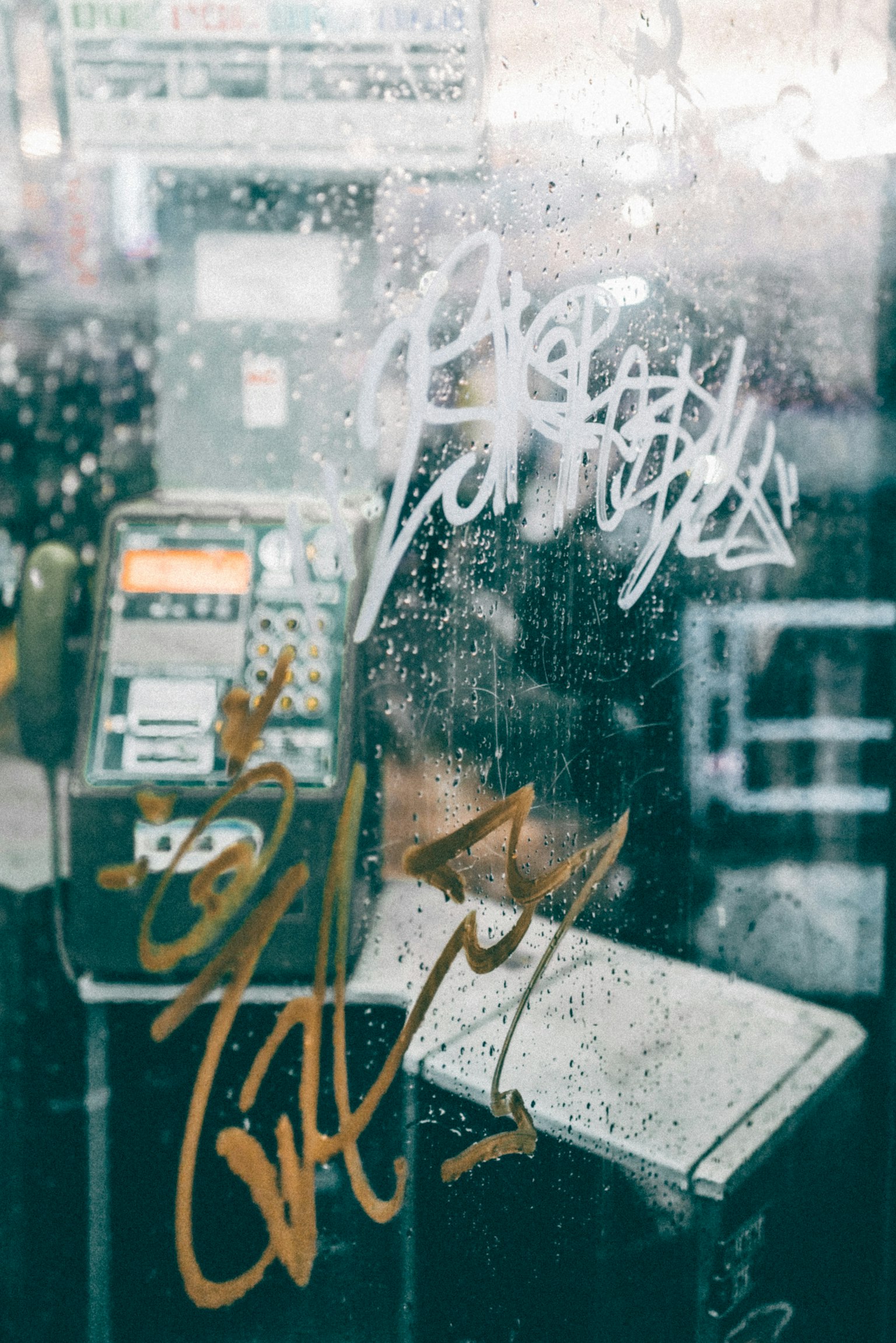 Graffiti on wet glass with a glimpse of a phone booth interior